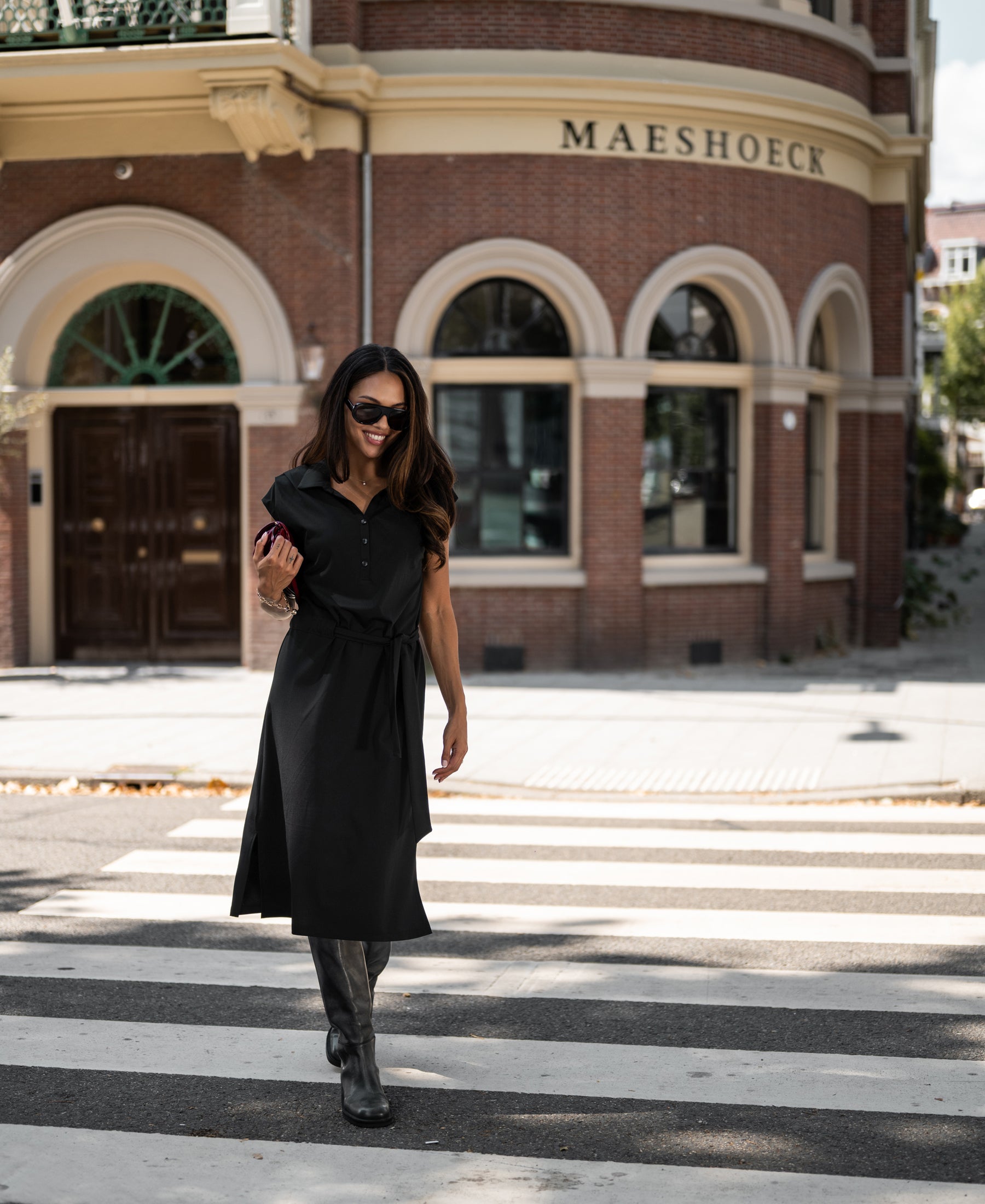 Woman wearing PLEIN PUBLIQUE’s black INES Travel polo dress, shown on a sunny day.
