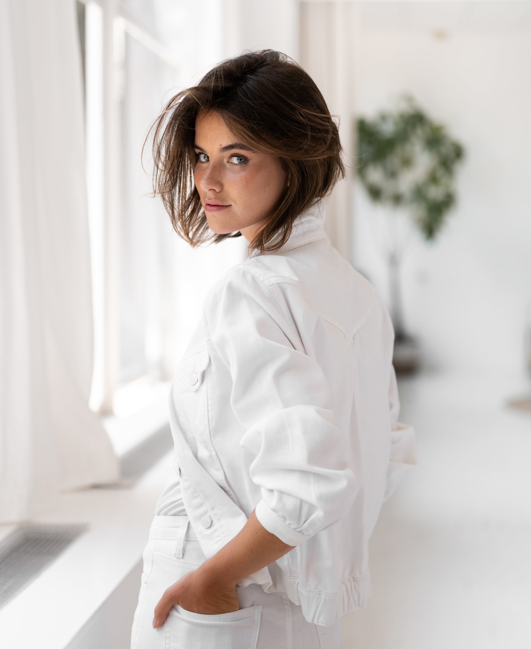 White denim jacket LA JACKY from PLEIN PUBLIQUE shown worn, back and side view, in a bright minimal room.
