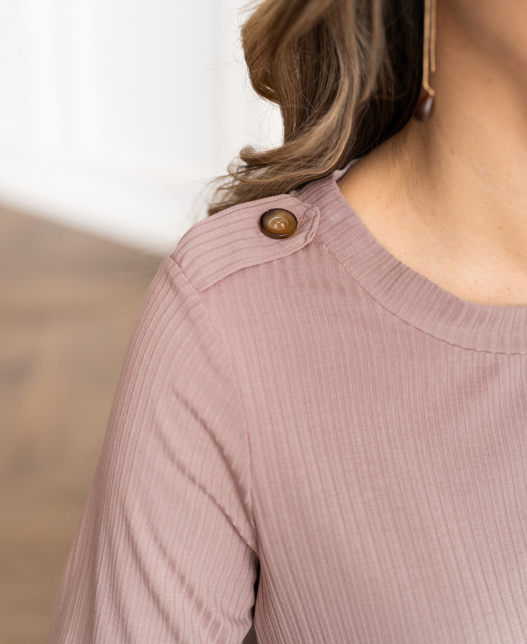 Woman in a bamboo T-shirt, dusty pink, with brown shoulder buttons.