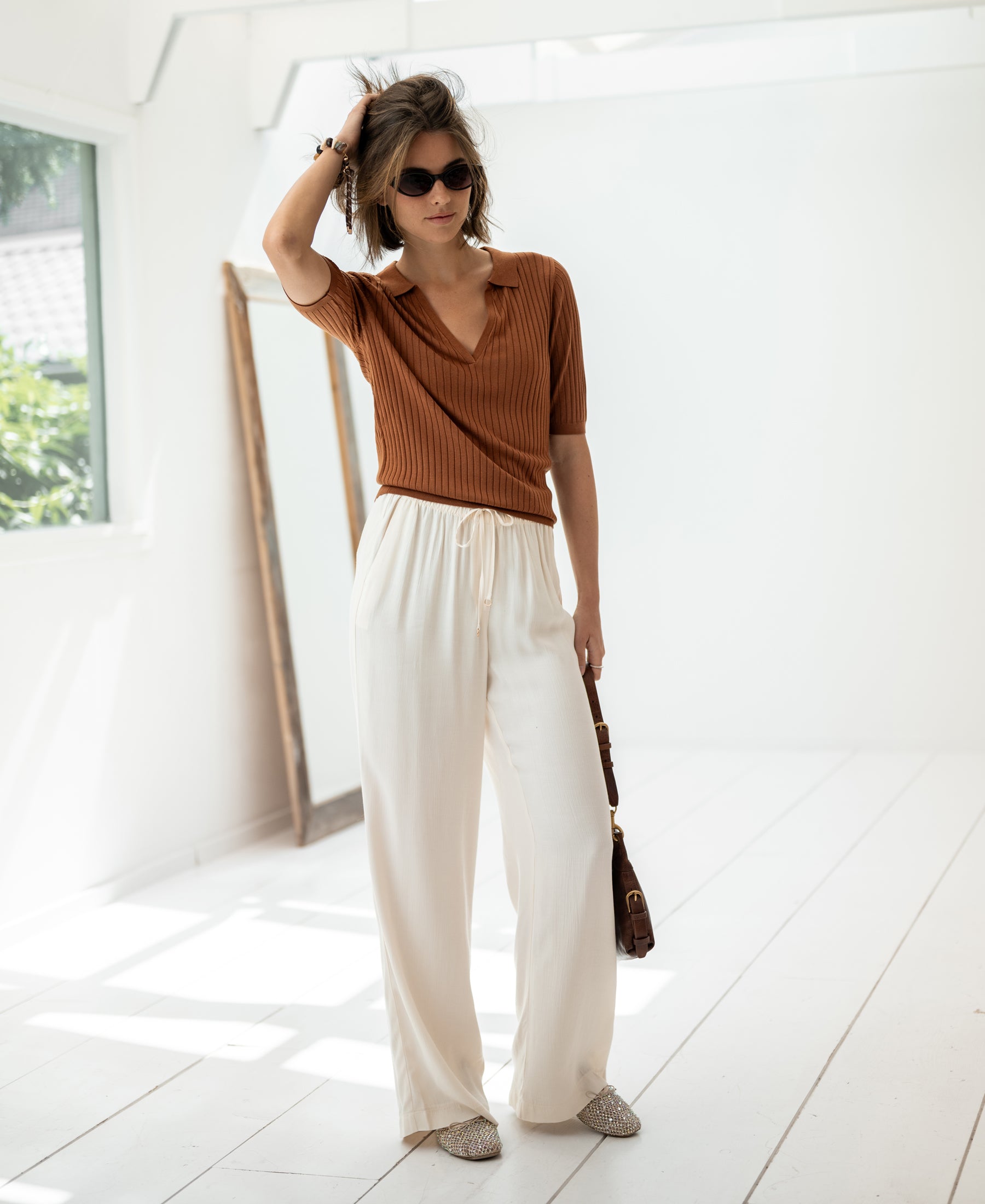 Woman wears the pleated public Tencel-silk polo shirt in Havana brown.
