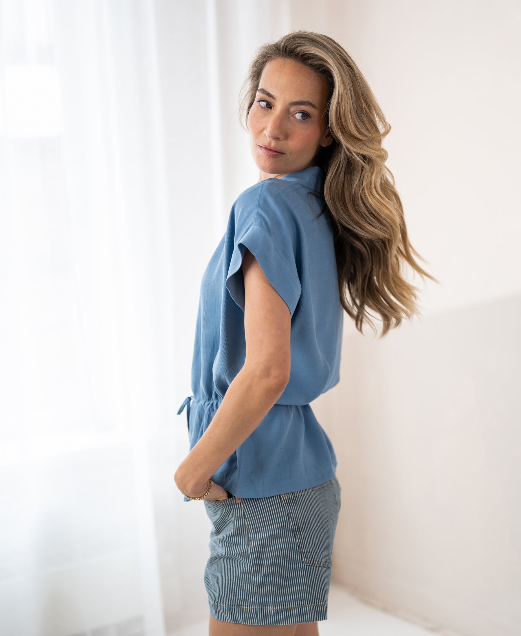 Blue LA JODY blouse by OVERIG, chic waist accent visible, shown from the side.