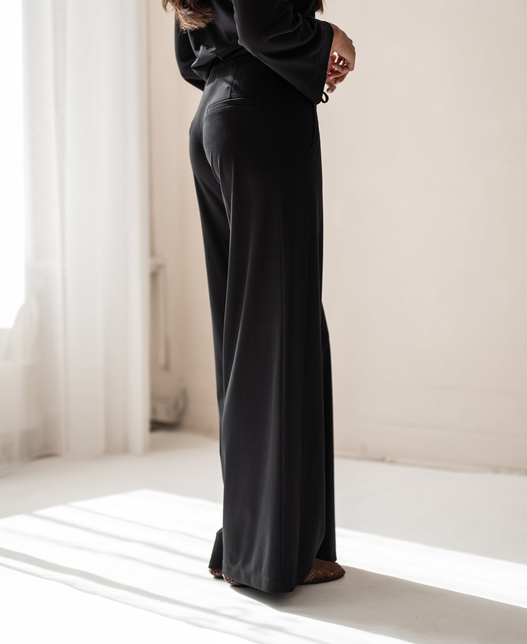 Black LA JULIA travel pants by PLEIN PUBLIQUE shown from the side.