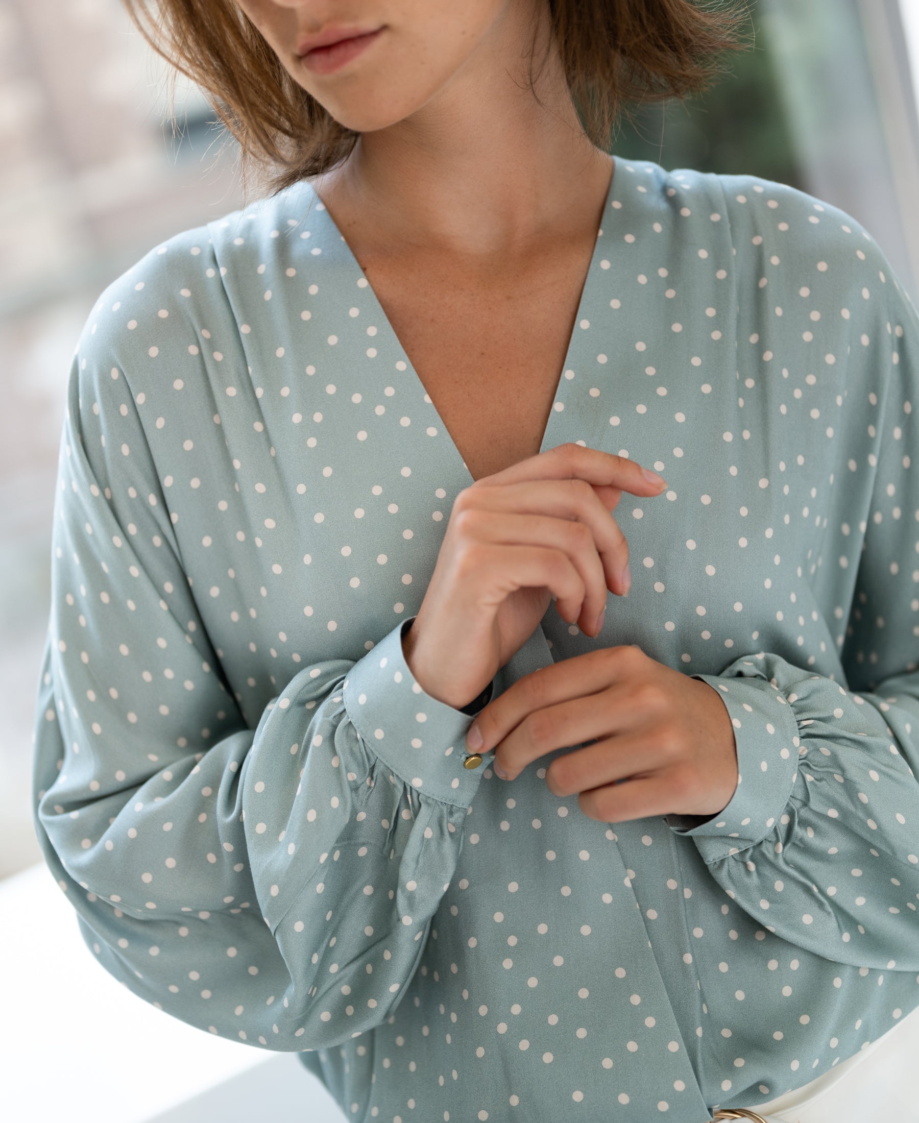 Light green and ivory wrap blouse with polka dots and puffed sleeves, shown indoors.