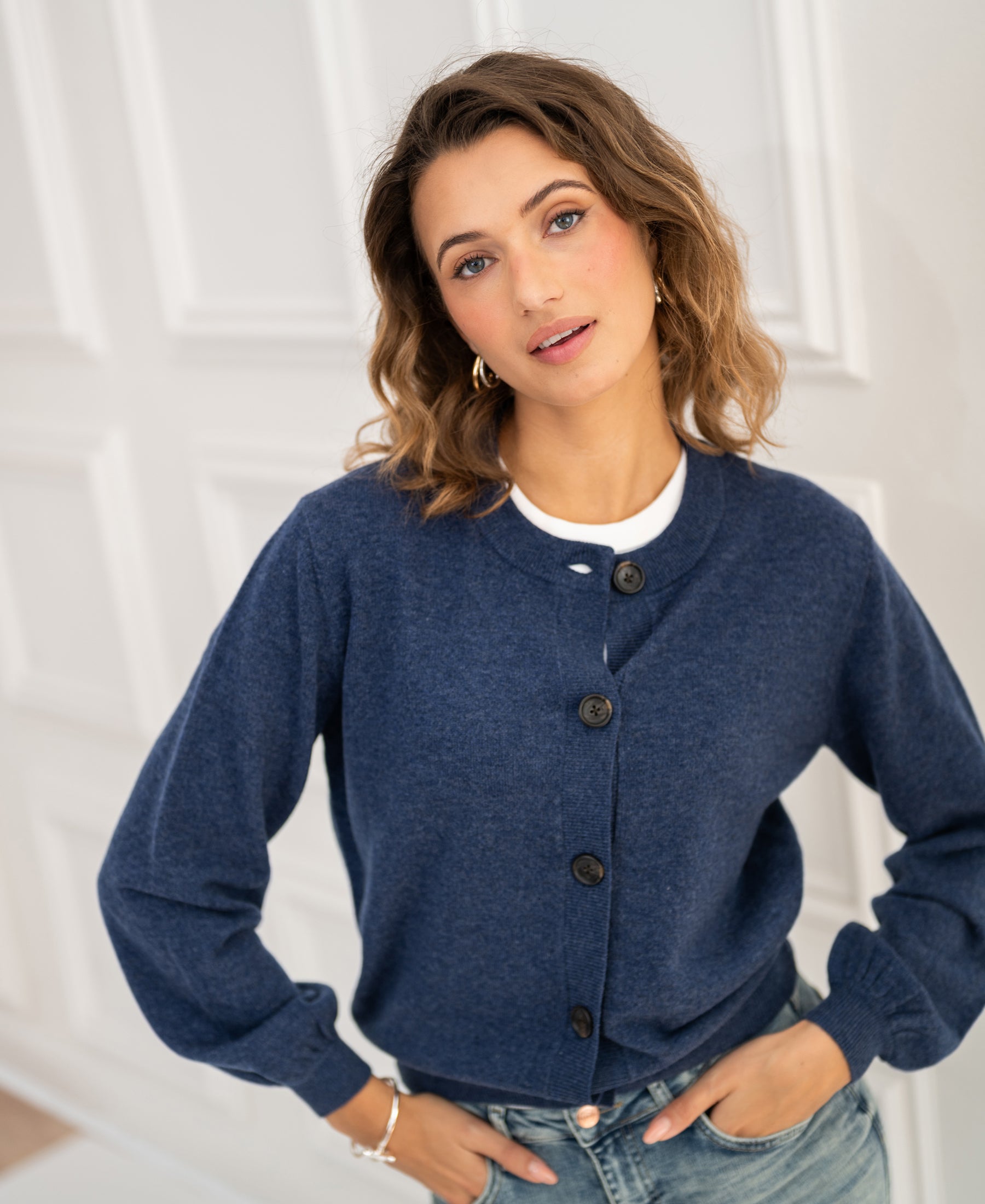 Indigo blue round neck vest by Plein Publique, LA LEA style, shown on a woman in front of a white paneled door.
