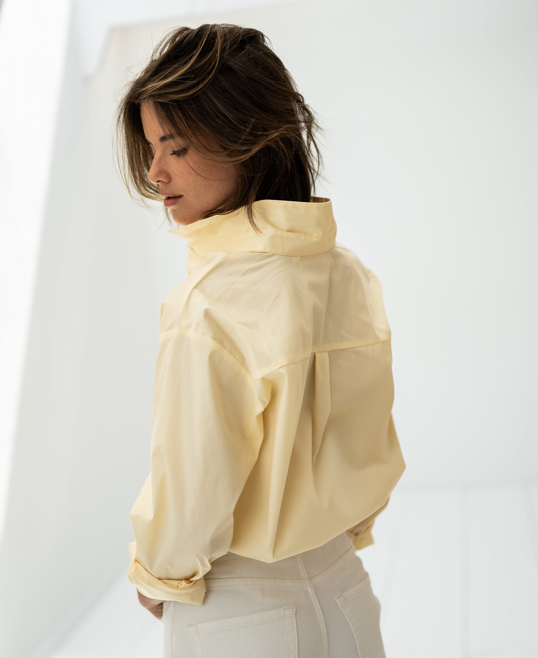 Woman wearing an oversized easy-iron blouse in soft yellow by PLEIN PUBLIQUE, looking down.