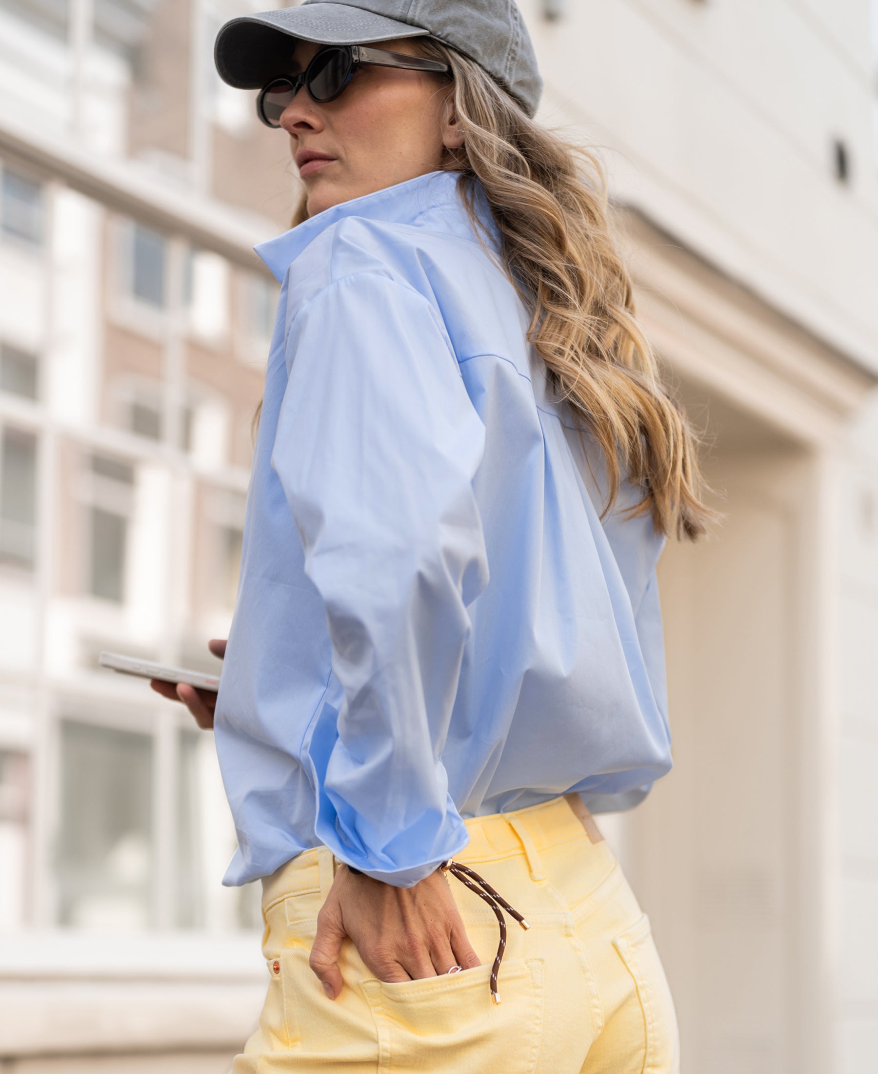 Woman wearing oversized easy-iron light blue blouse stands outdoors.