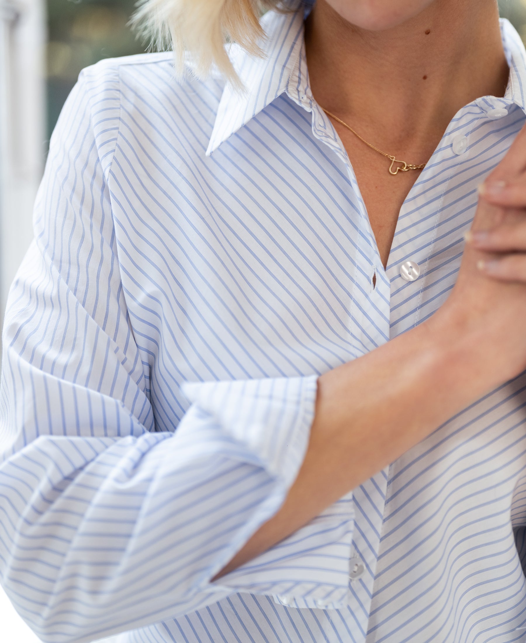 Woman wearing striped blouse in white and light blue, partial face visible, arms crossed.
