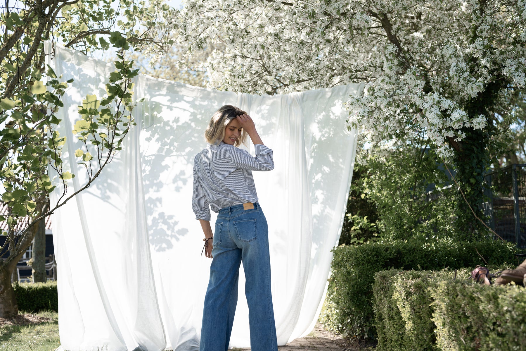 Back view of woman wearing white and black striped PLEIN PUBLIQUE LA LOIRE blouse outdoors.