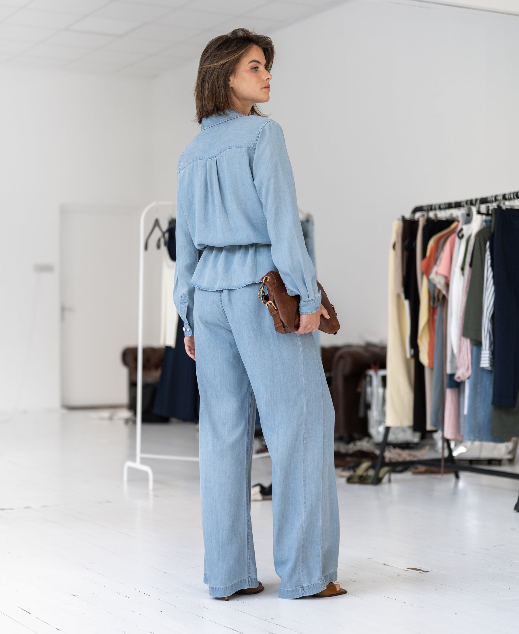 Woman wearing a bleached Tencel denim blouse stands in a minimal boutique.
