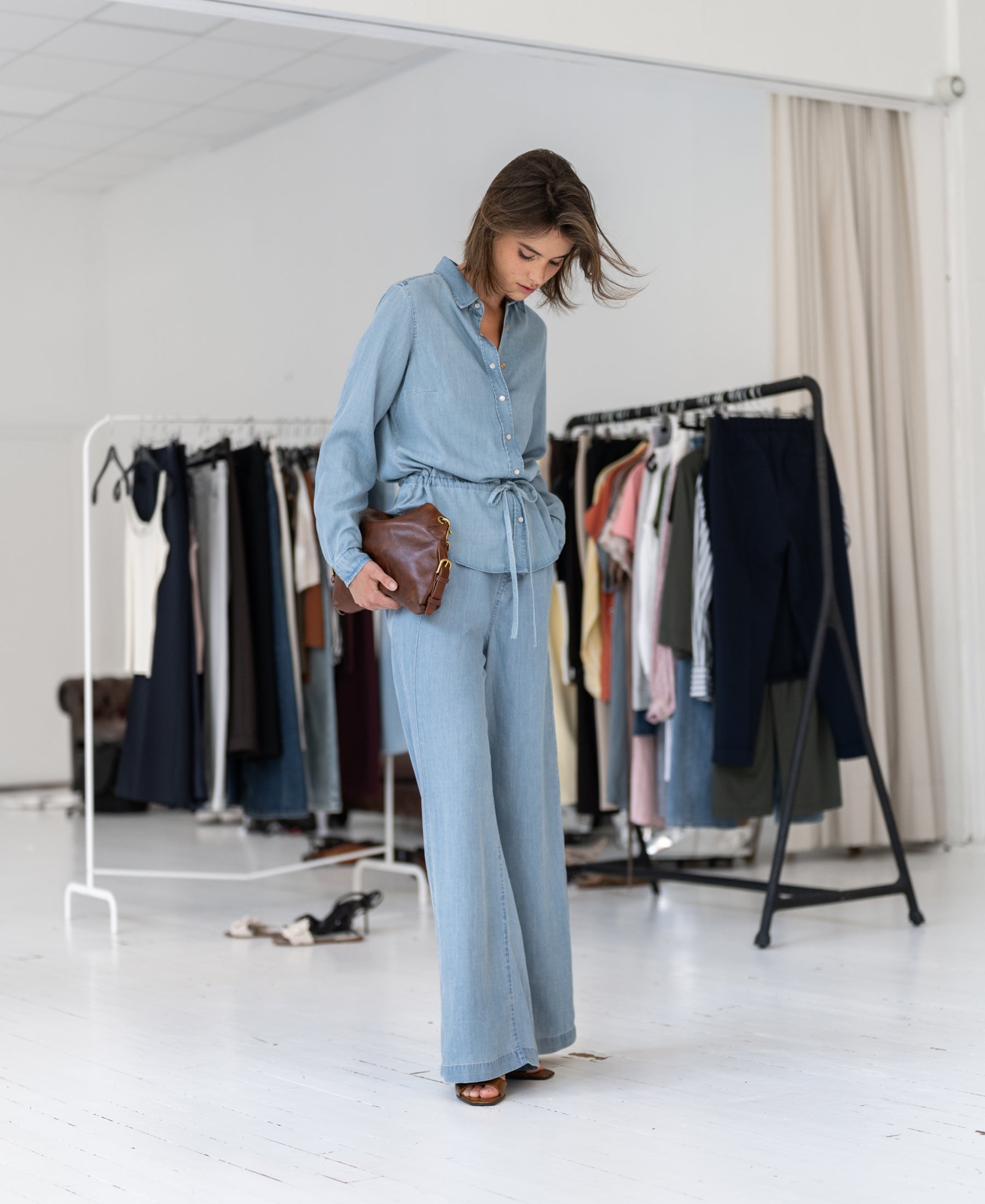 Front view of woman wearing a Tencel denim blouse by PLEIN PUBLIQUE in a bright room.