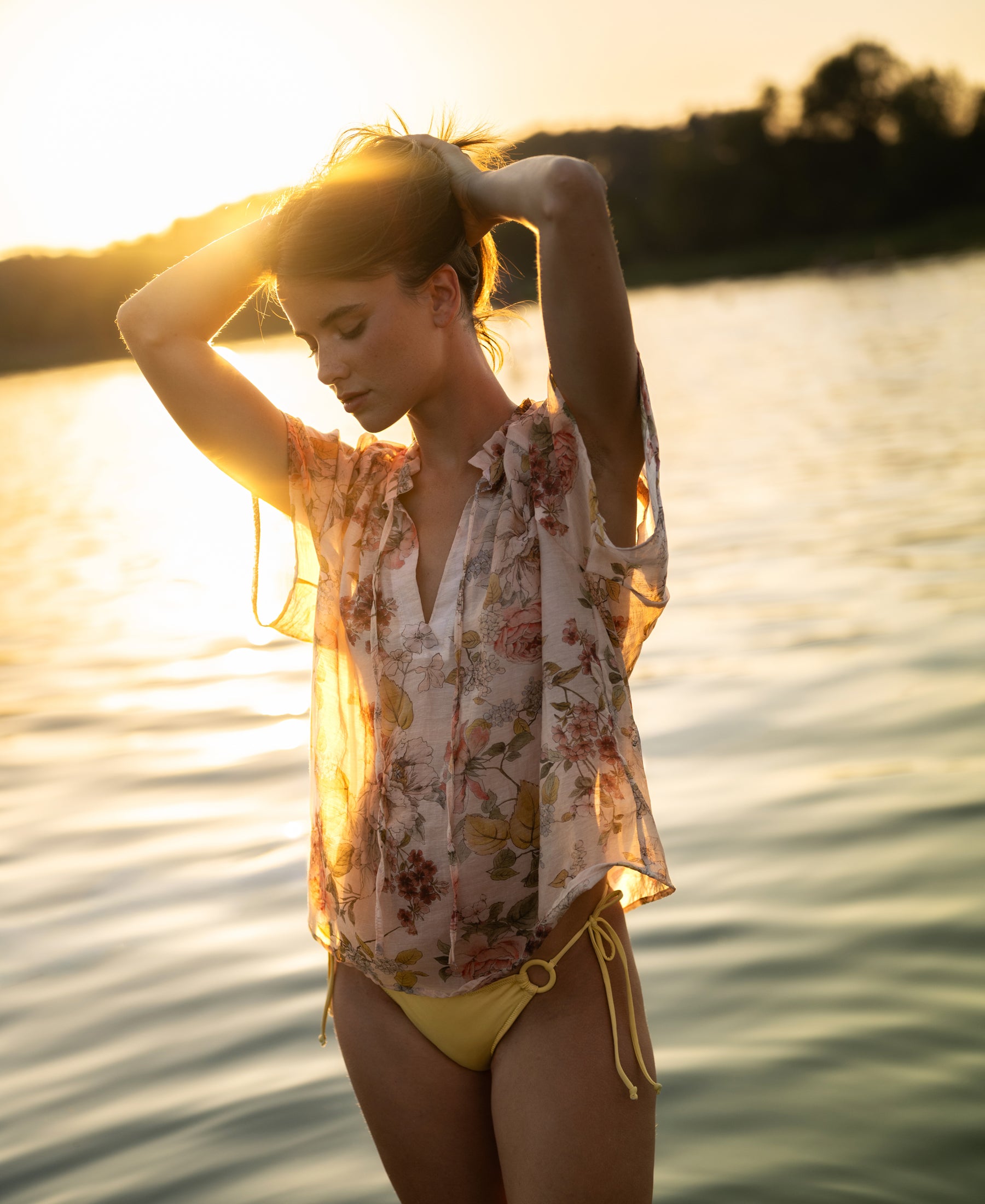 Blush floral-print blouse by PLEIN PUBLIQUE shown outdoors at sunset, front view.