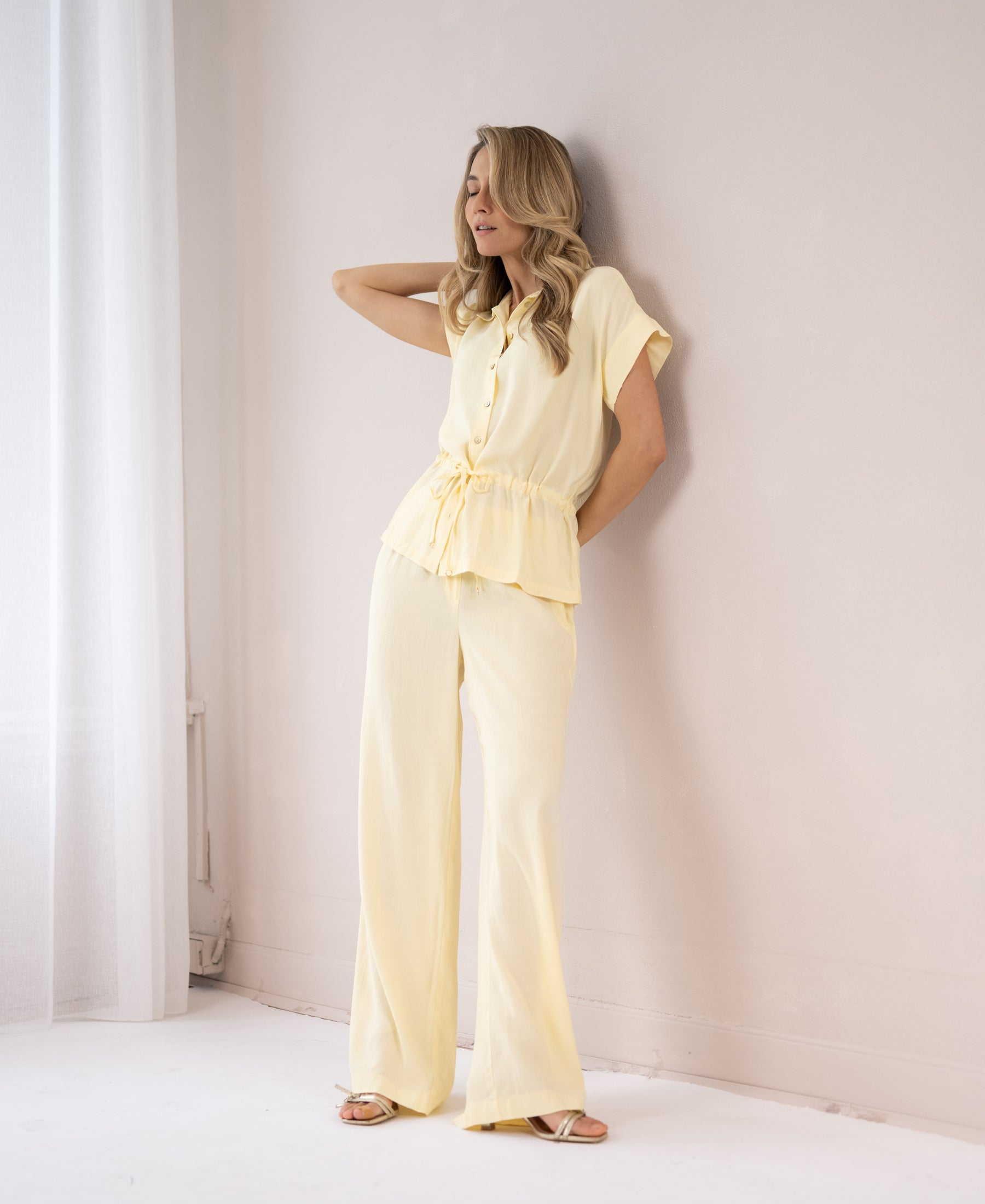 Light yellow LA LYNETTE pants shown on a woman standing against a white wall.