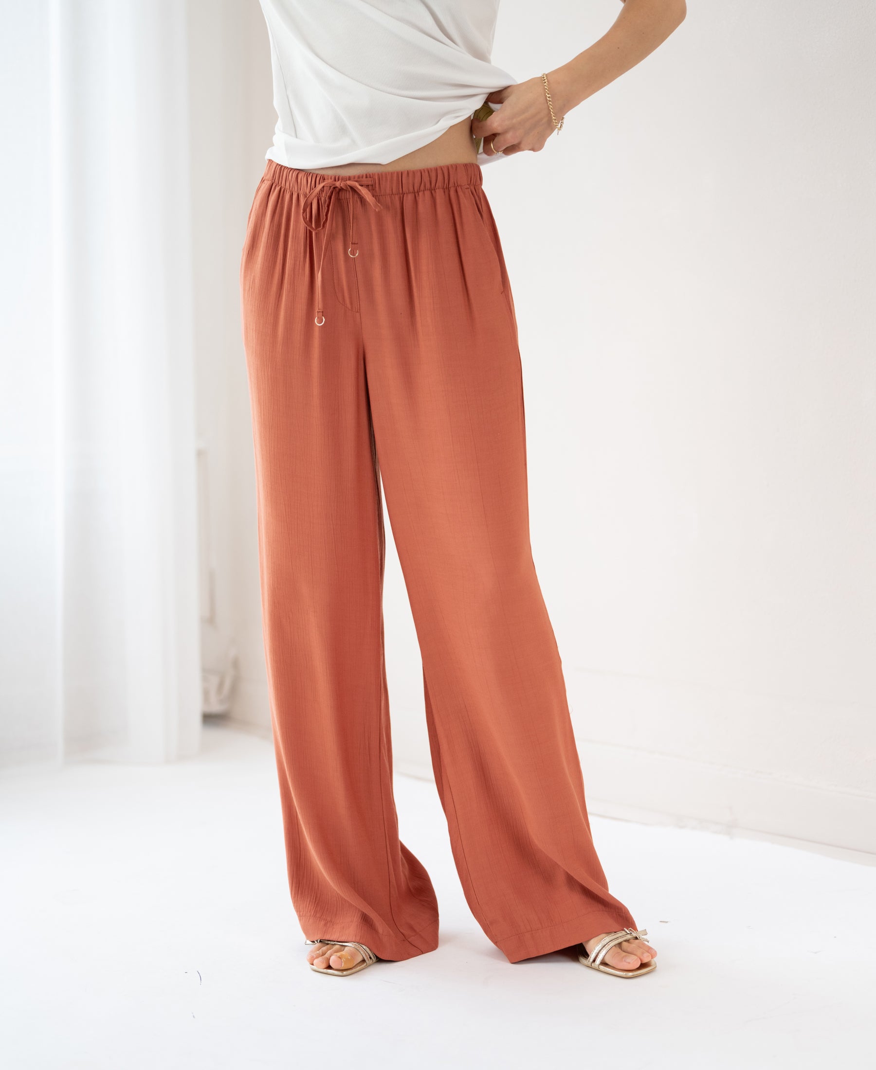 Wide leg terra-colored pants with a stretch waist, shown in a bright, minimalist room.