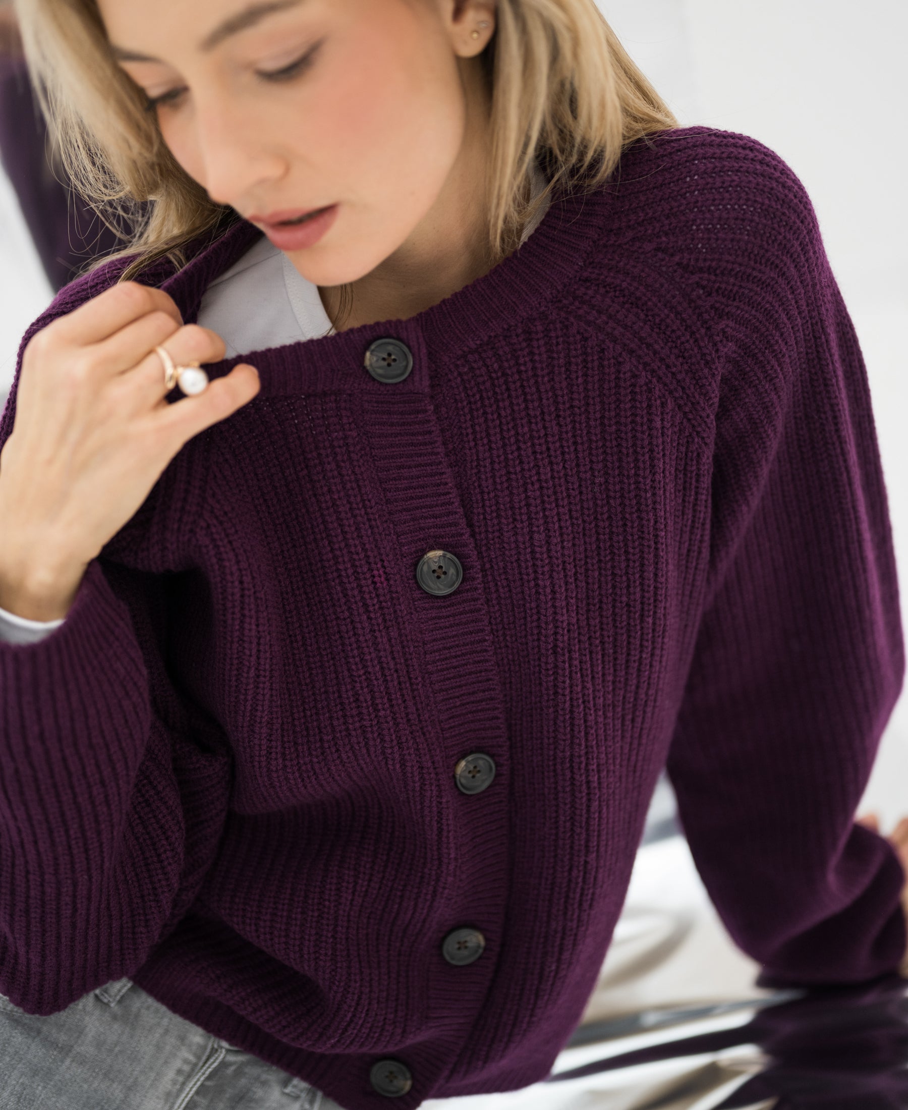 Merino wool vest in Cassis color, front view with model holding the collar and looking downward.