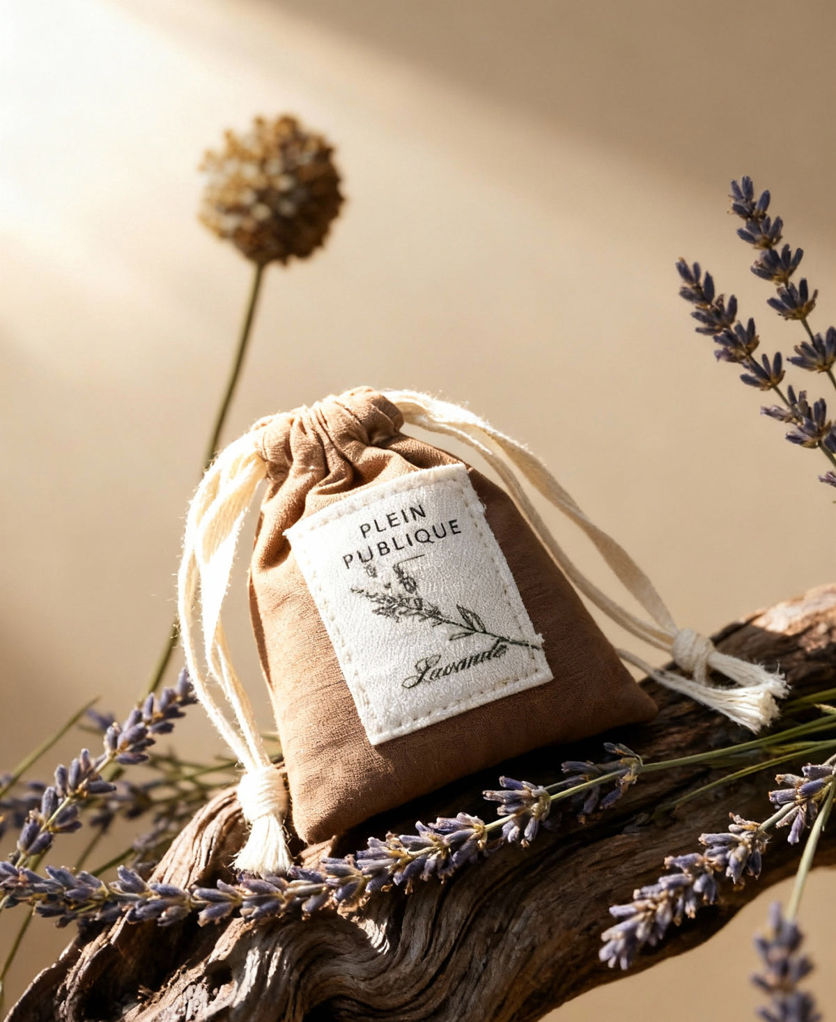 A small brown lavender sachet by PLEIN PUBLIQUE lies on wood with lavender.