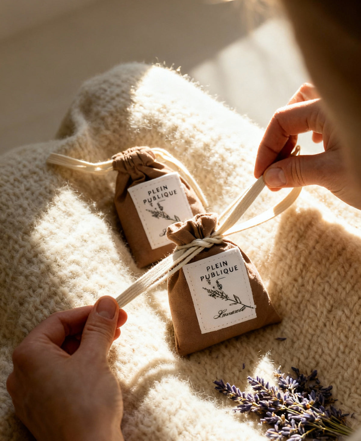 Hands tying a ribbon on a PLEIN PUBLIQUE Lavender Scented Sachet—ideal for keeping moths out of your wardrobe.