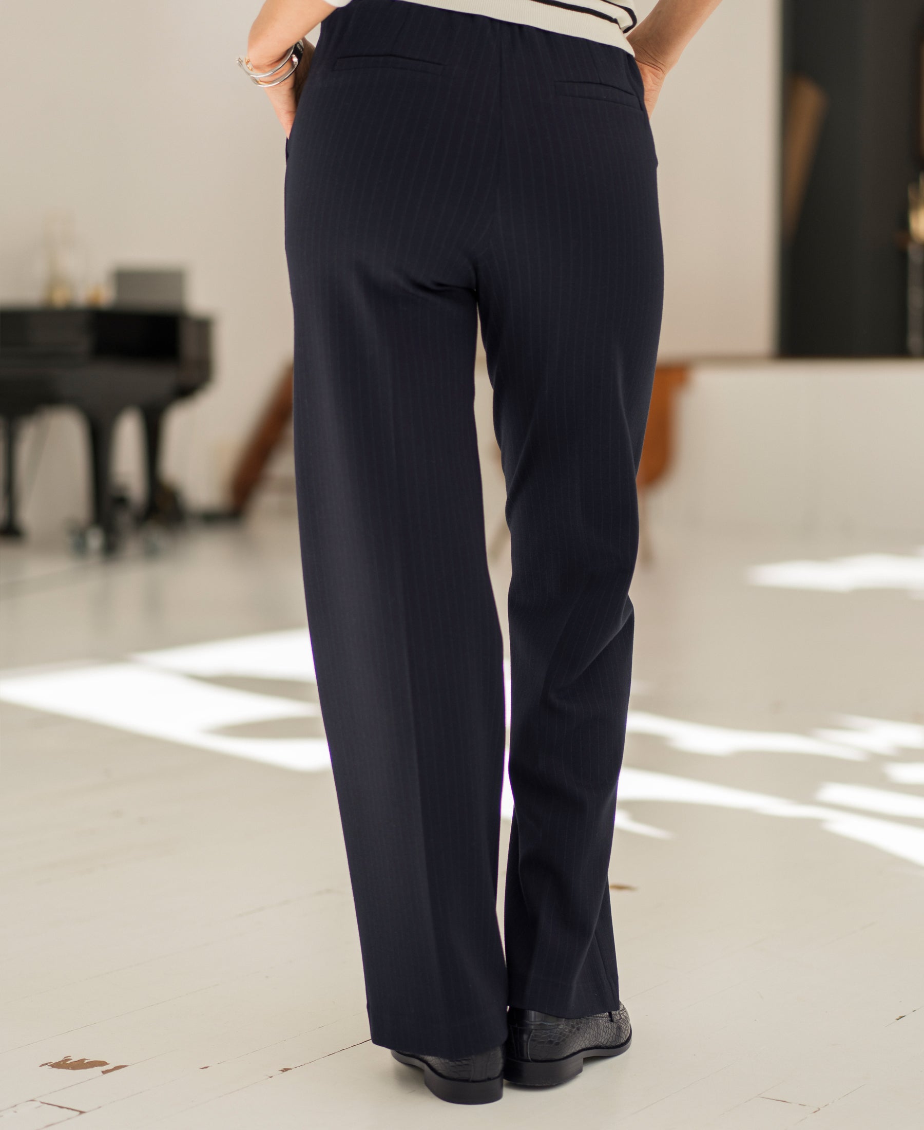 Back view of person indoors wearing navy pinstripe LE MALO trousers by Plein Publique.