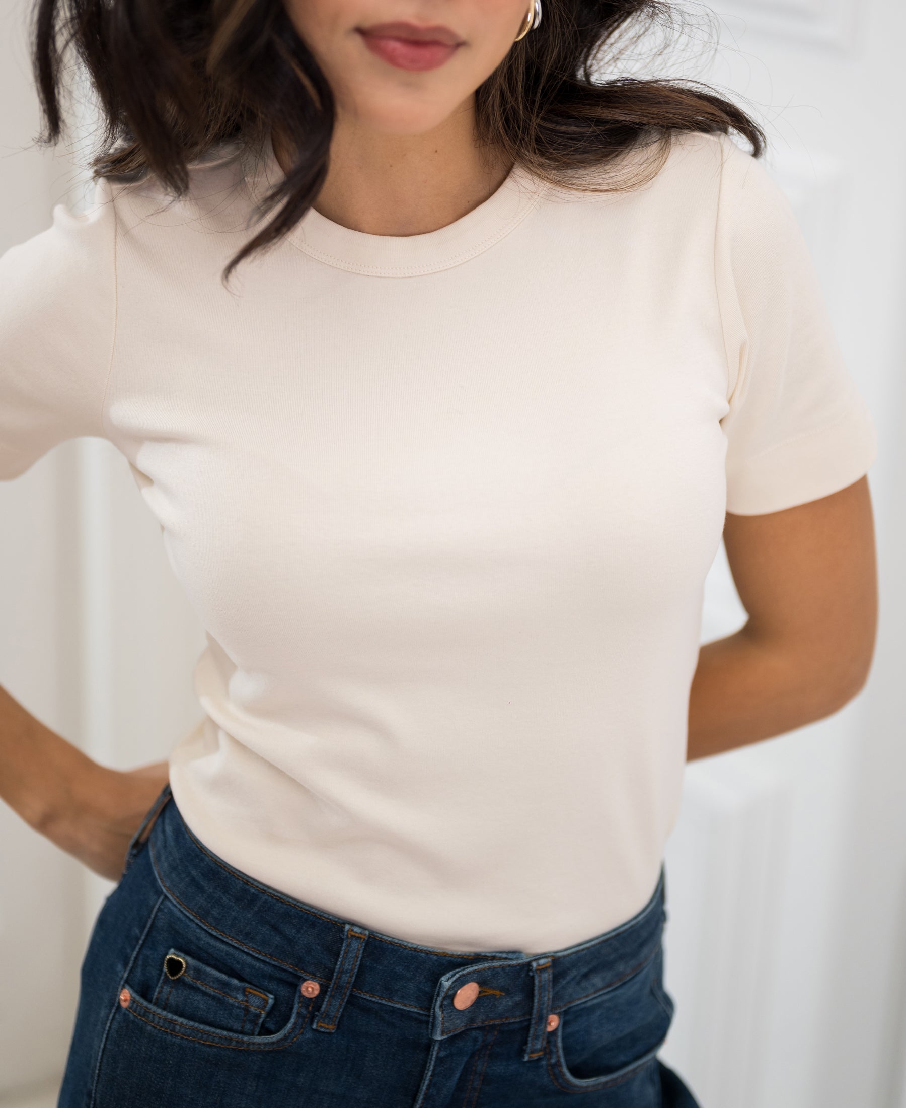 Woman wears the PLEIN PUBLIQUE soft butter-colored T-shirt, hands on hips.