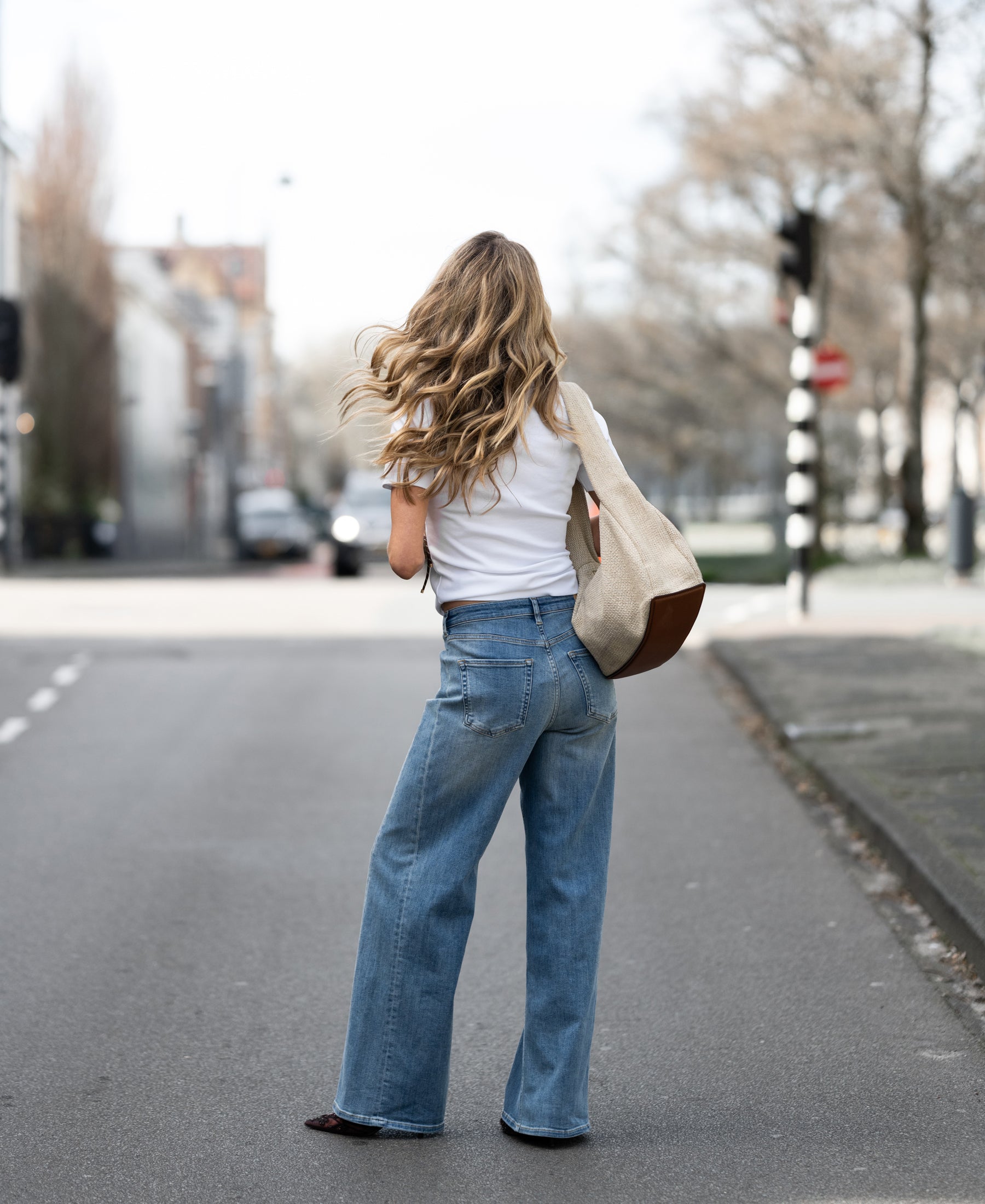 Wide leg jeans in light stone wash, shown from the back as the model stands facing away in an empty street.