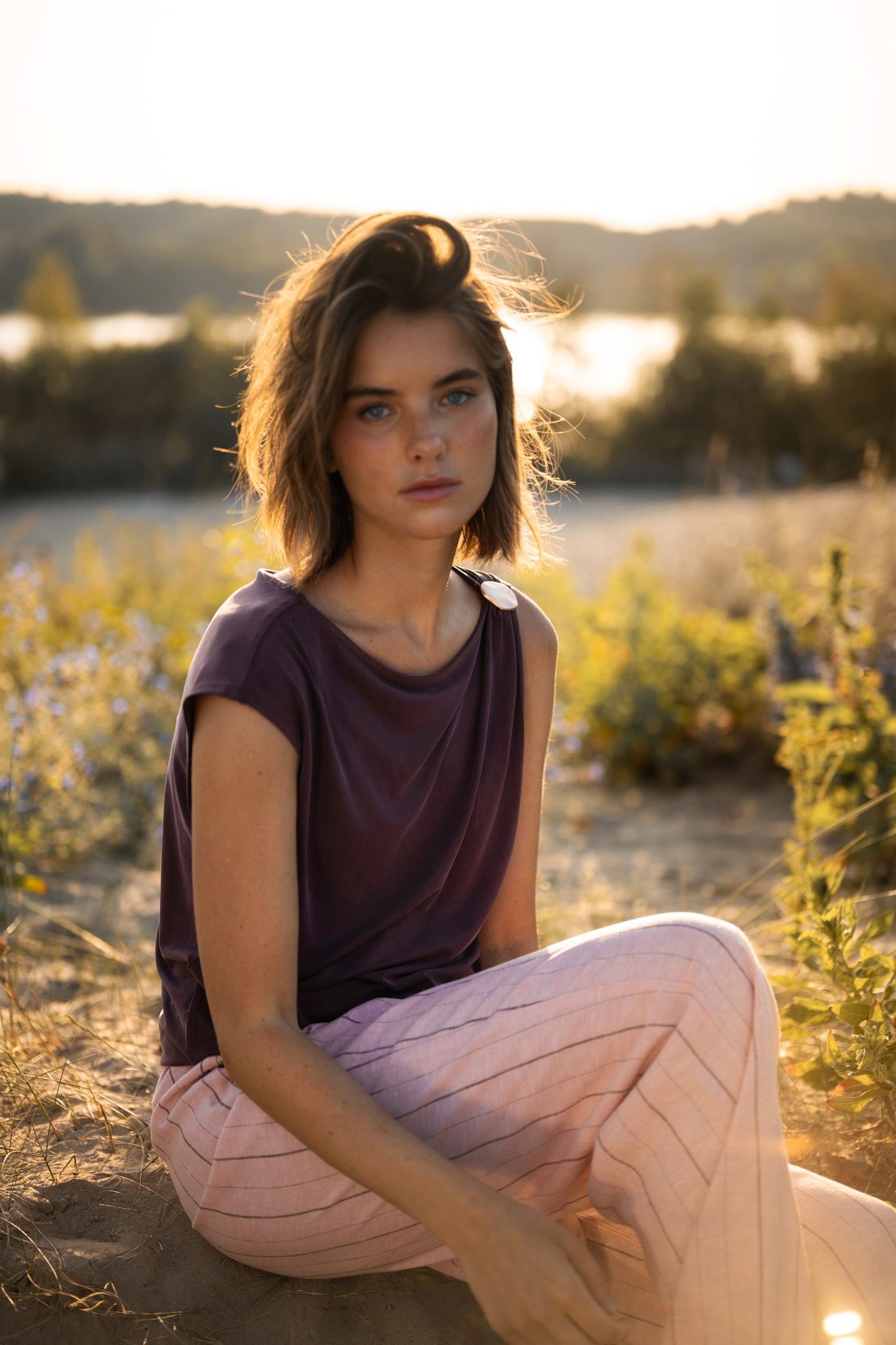 Wine-colored PLEIN PUBLIQUE LA MAYA top with buckle detail, shown on a woman sitting outdoors.