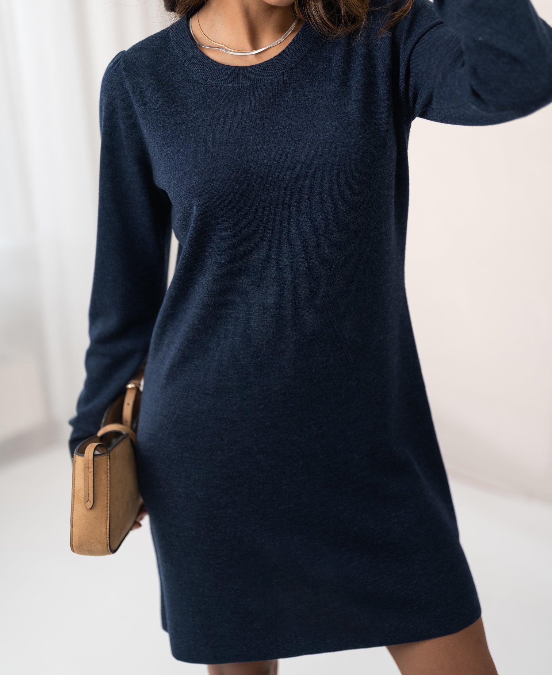 Woman wearing a denim blue LA MIMI merino wool dress by PLEIN PUBLIQUE indoors against a light background.