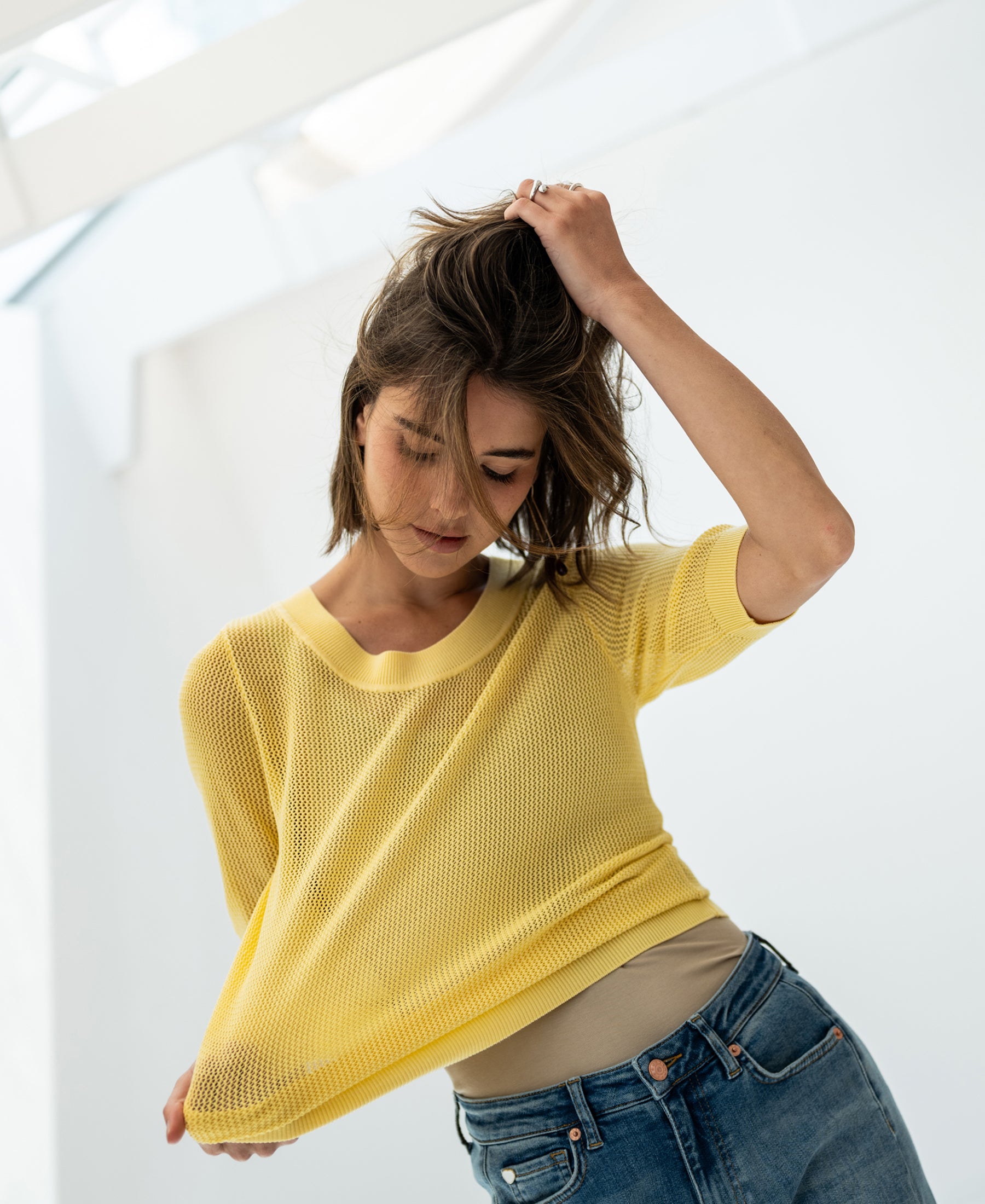 Woman wearing yellow mesh silk sweater indoors, lifting her hair.