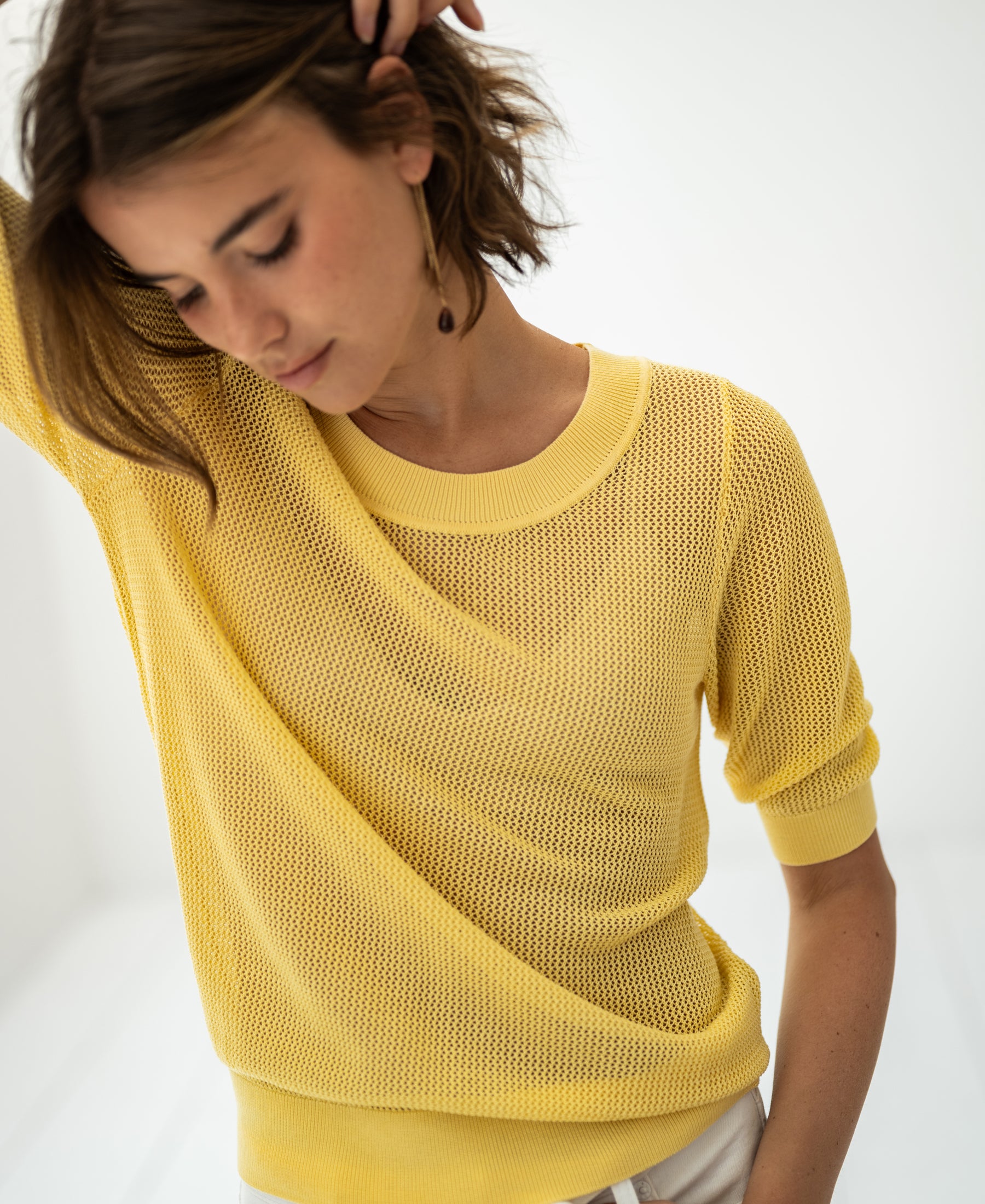 Citron yellow mesh sweater with silk, front view. Model poses with head down and arm raised.