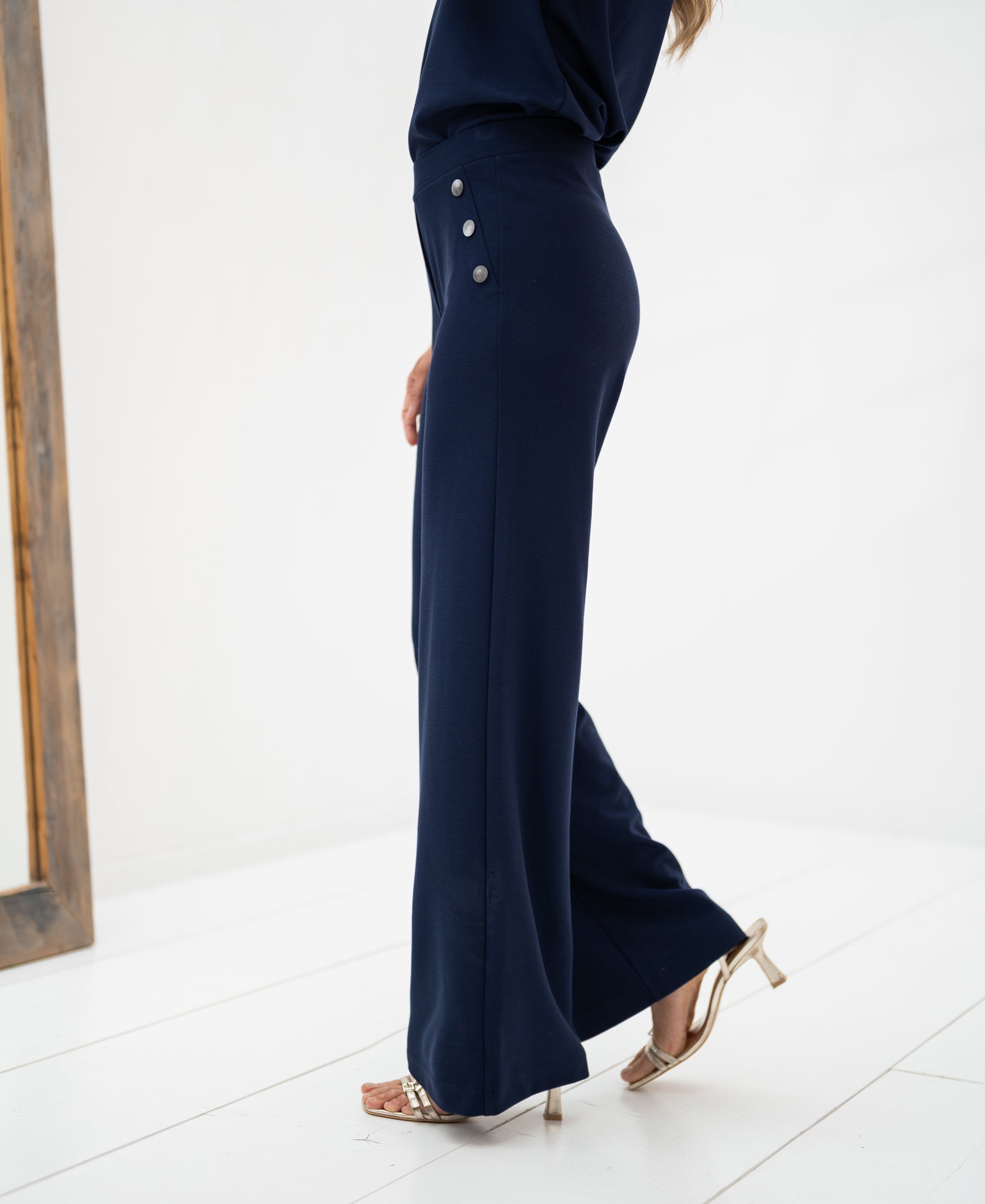 Side view of dark blue travel pants on a woman, shown on a white floor.