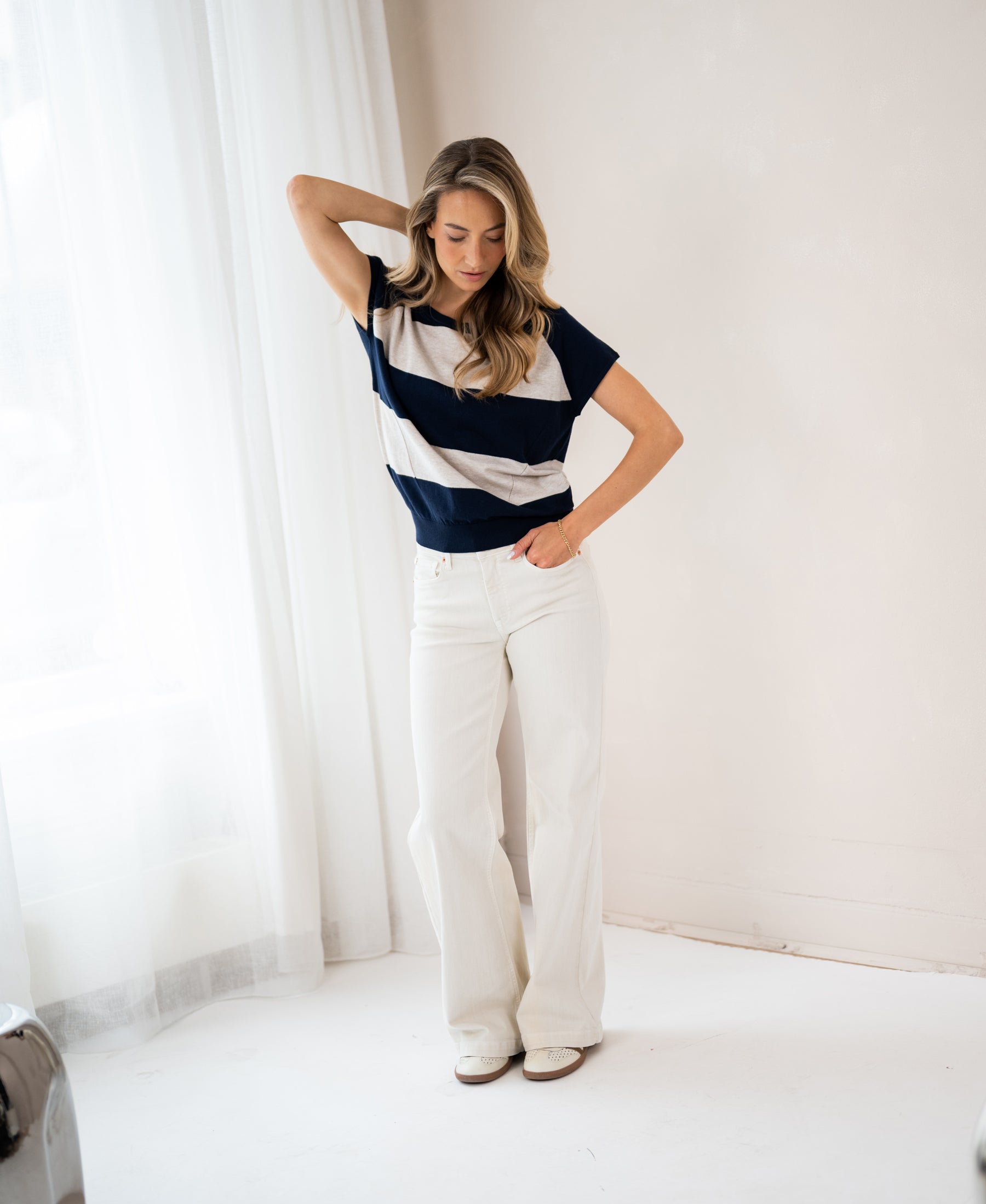 Woman wearing a navy and sand striped sweater, looking down with one hand in her pocket.
