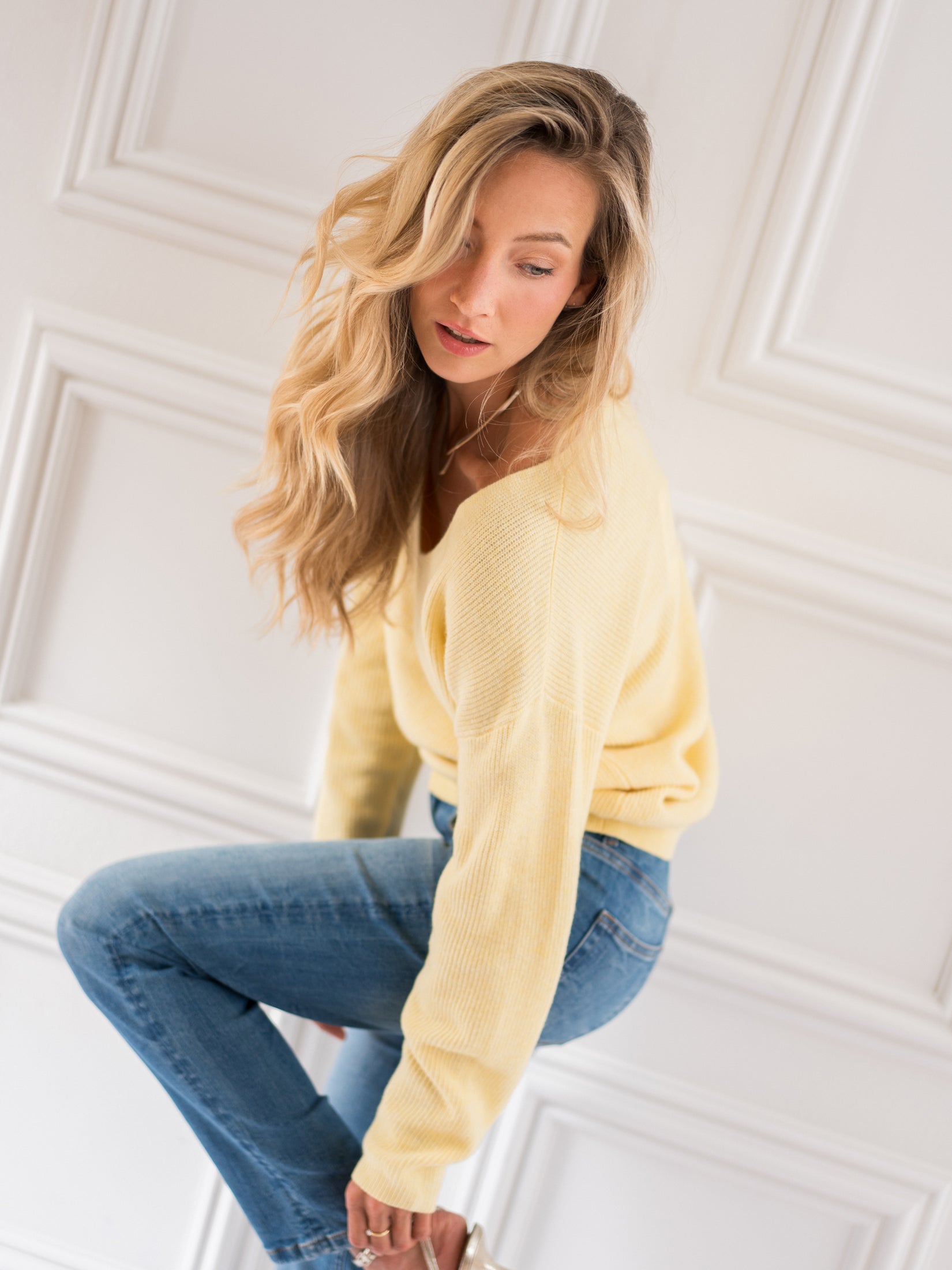 Yellow merino wool sweater posed against a white paneled wall.