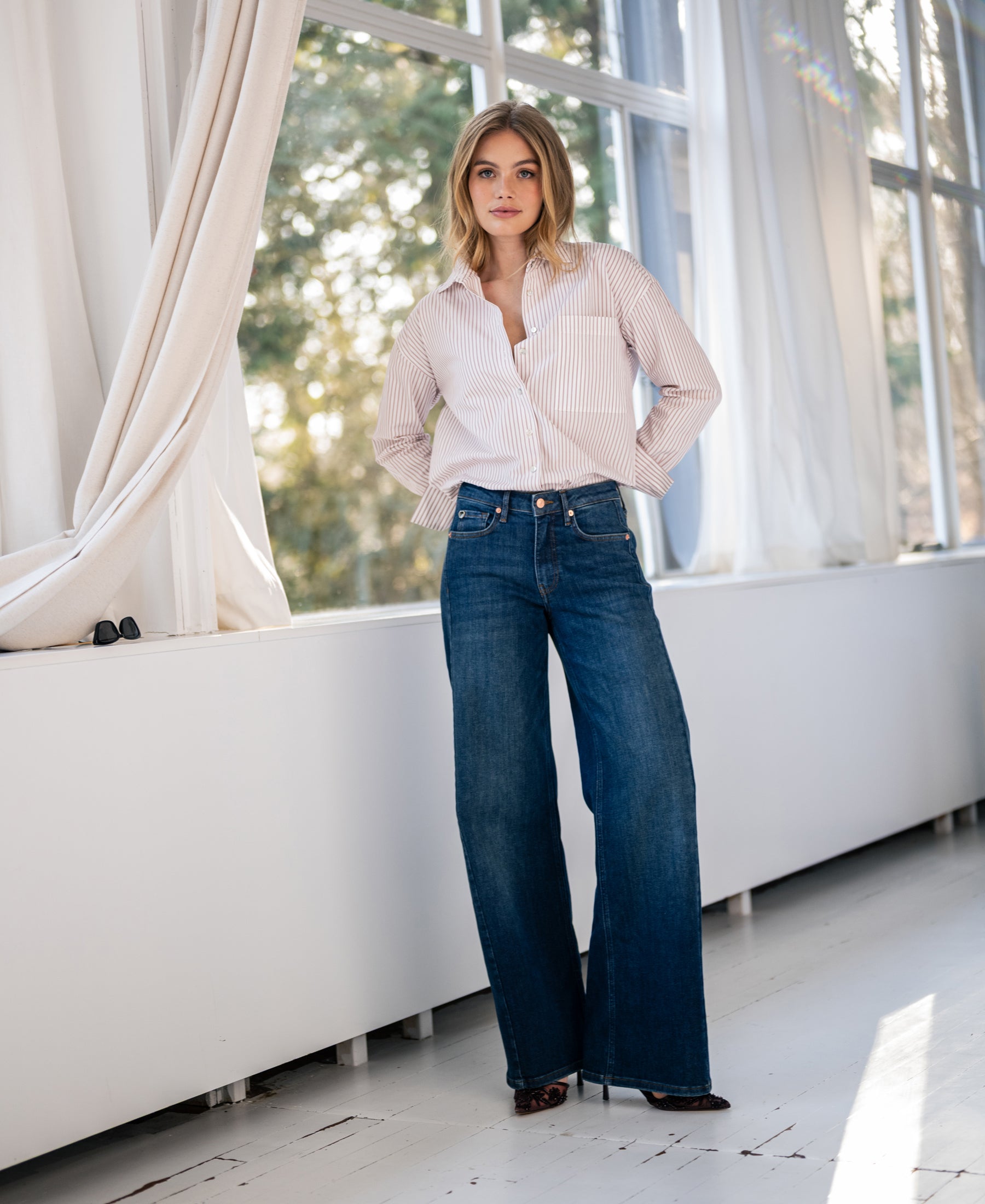 White and dark red striped blouse with long sleeves, worn indoors by large windows with light streaming in.