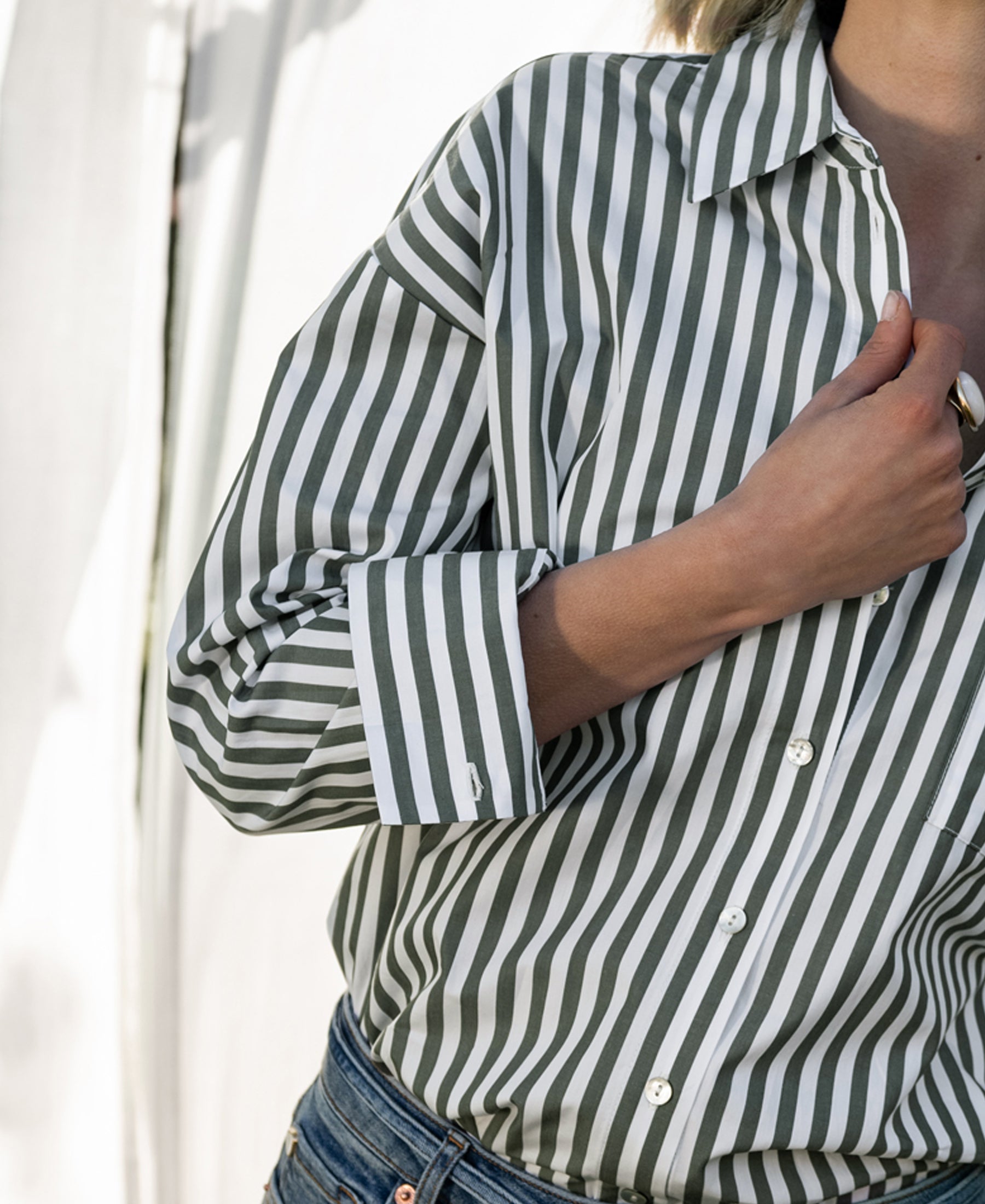 Woman wearing a white and olive green striped blouse, holding the collar.