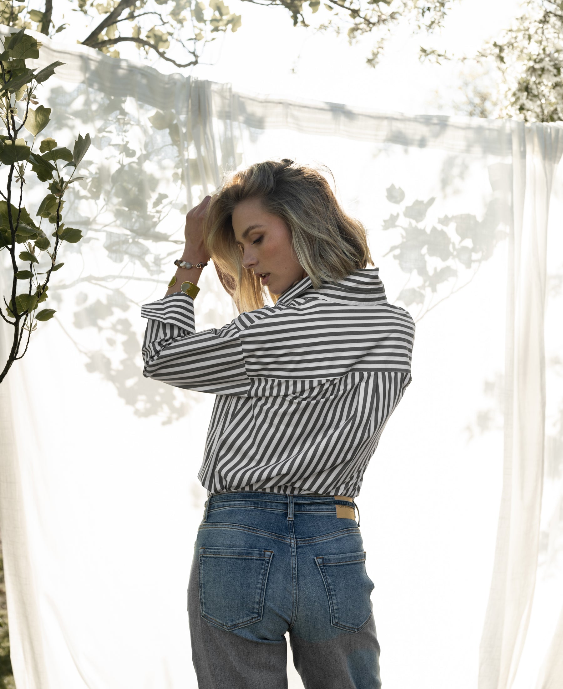 White and olive-green striped PLEIN PUBLIQUE LA PASCALLE blouse shown outside by a sheer white curtain.