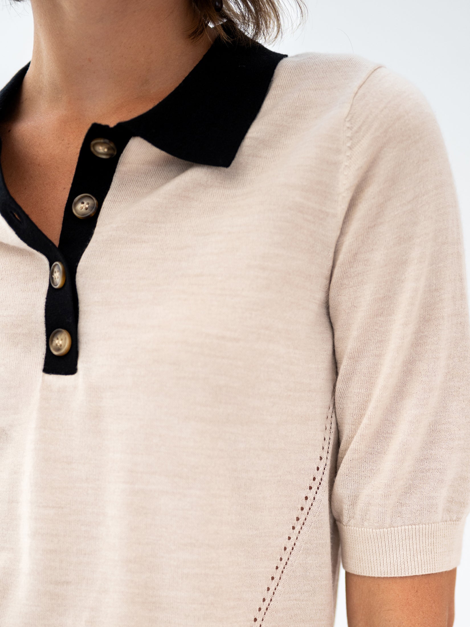 Close-up of a Merino wool-silk polo shirt in sand and black with a black collar and placket.