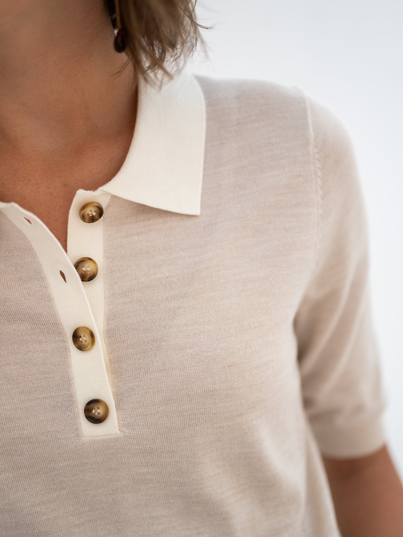 Close-up of a sand-ivory merino wool and silk polo shirt with brown buttons and short sleeves.