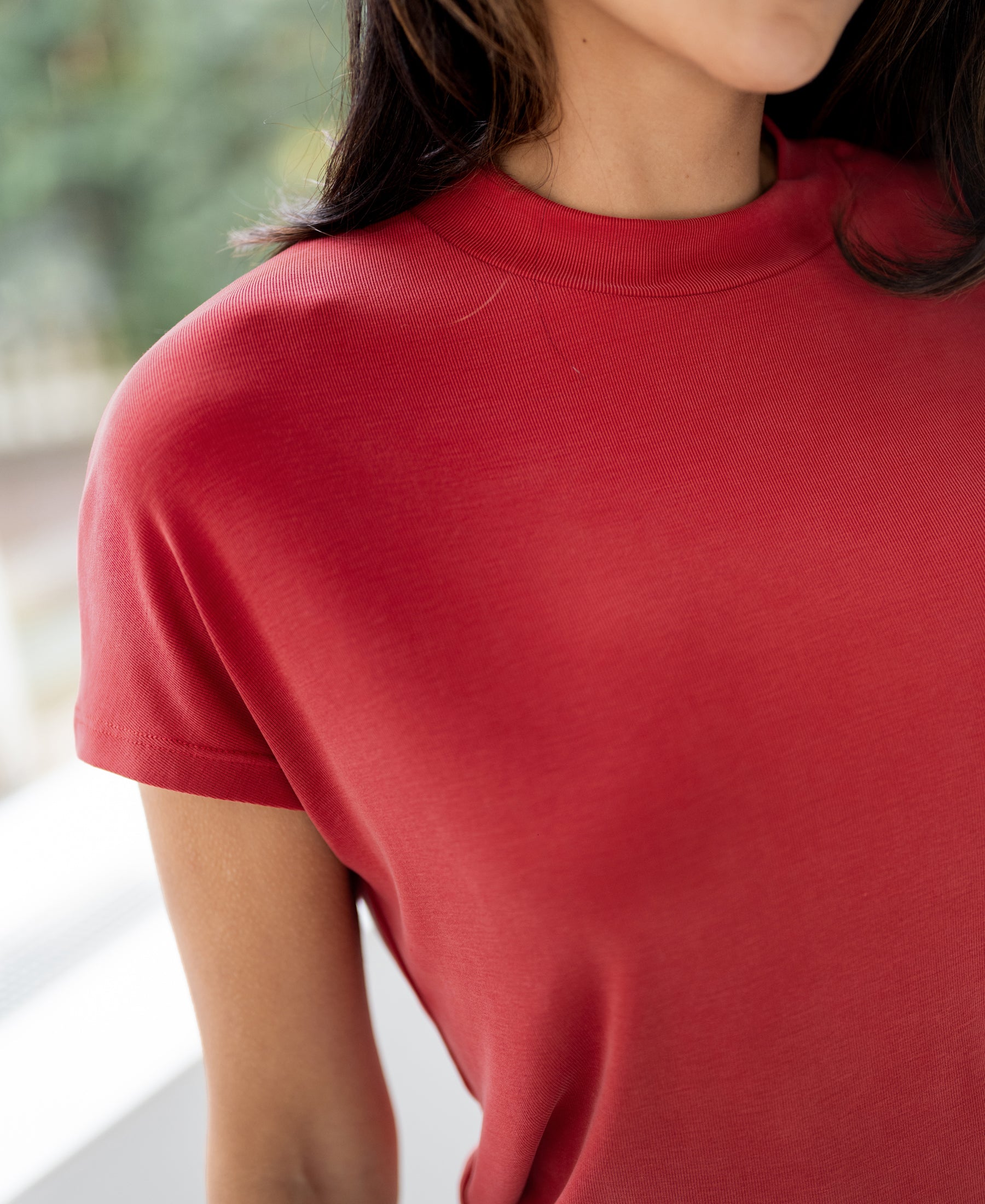 Red ribbed knit top, shoulder-up view, near a bright window.