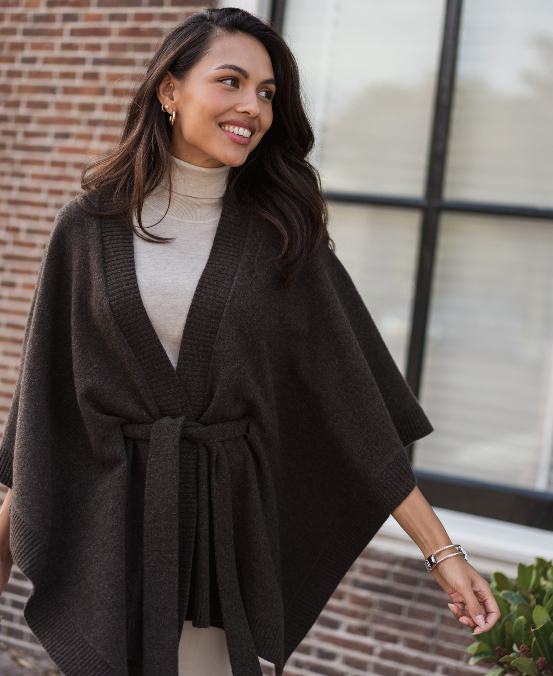 Chocolate brown merino wool poncho in an outdoor setting, shown against a brick wall and window.