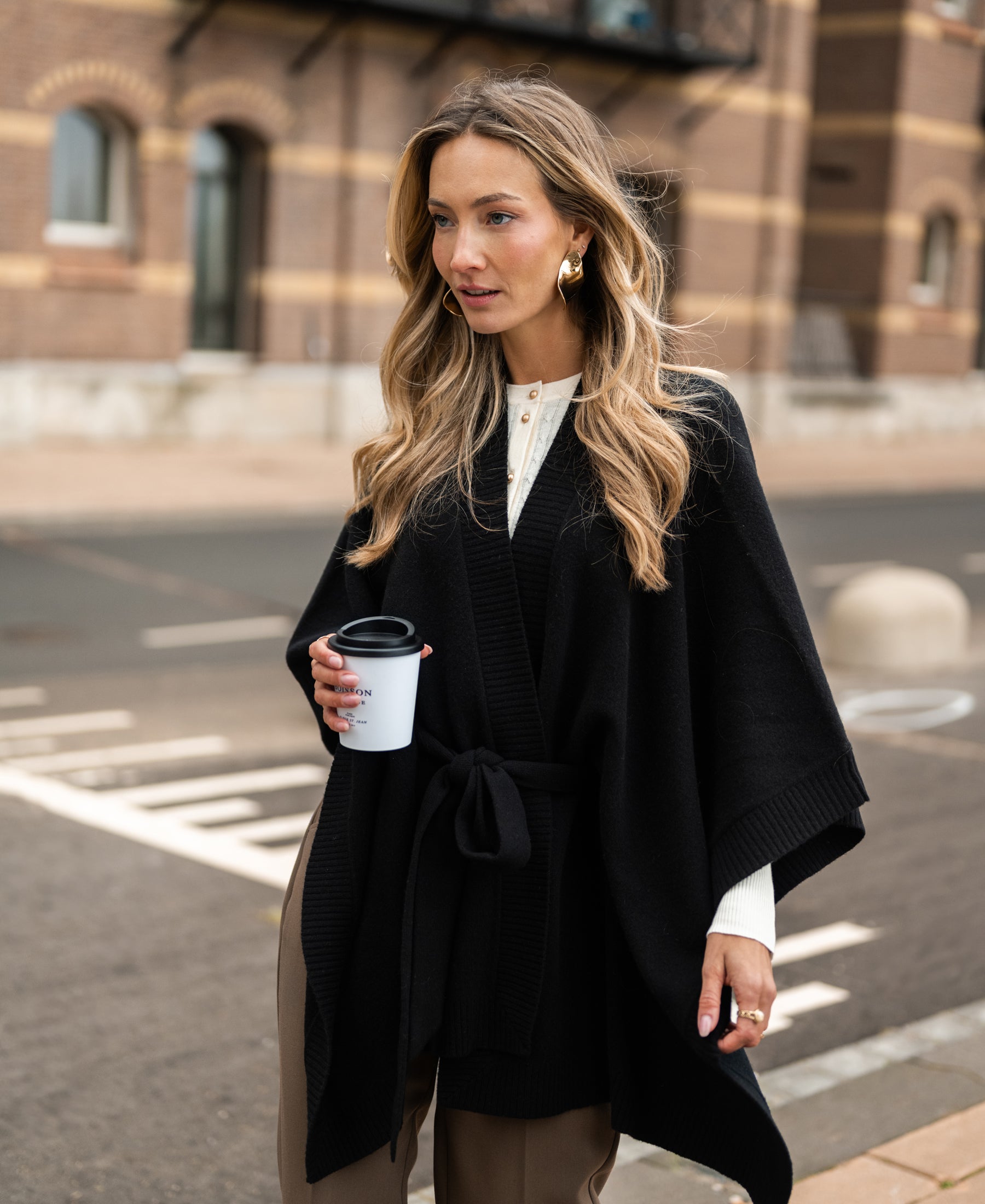 Black merino wool poncho by PLEIN PUBLIQUE shown outdoors.