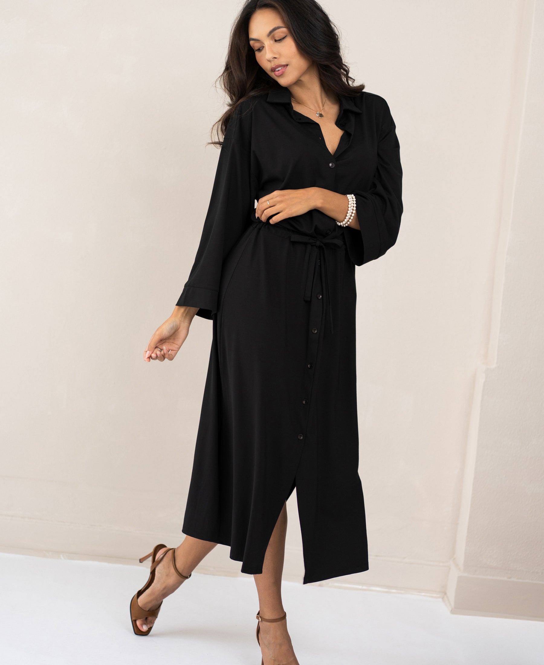 Woman wearing the PLEIN PUBLIQUE button-front dress LE RAPHAEL in black, standing against a light wall.