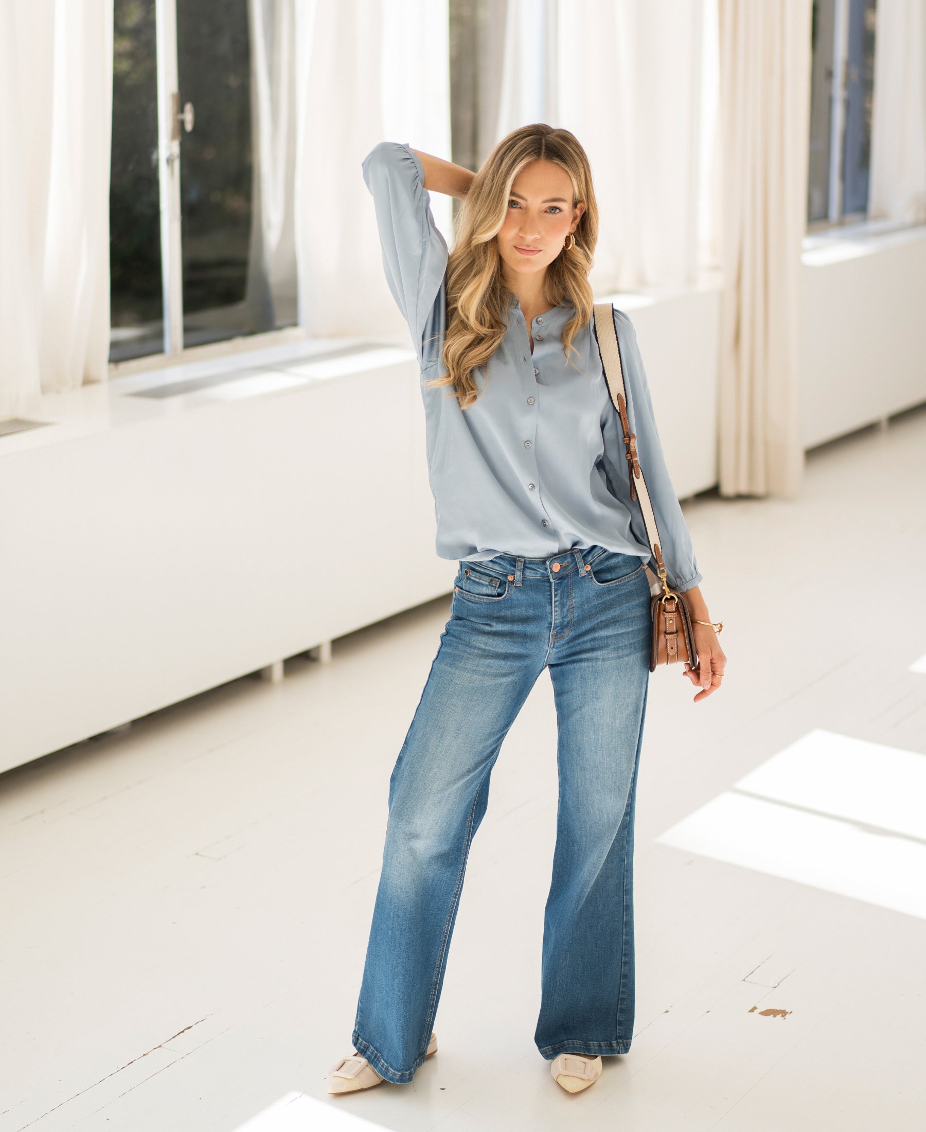 Woman in a bright room wears wide leg stonewash jeans from PLEIN PUBLIQUE.