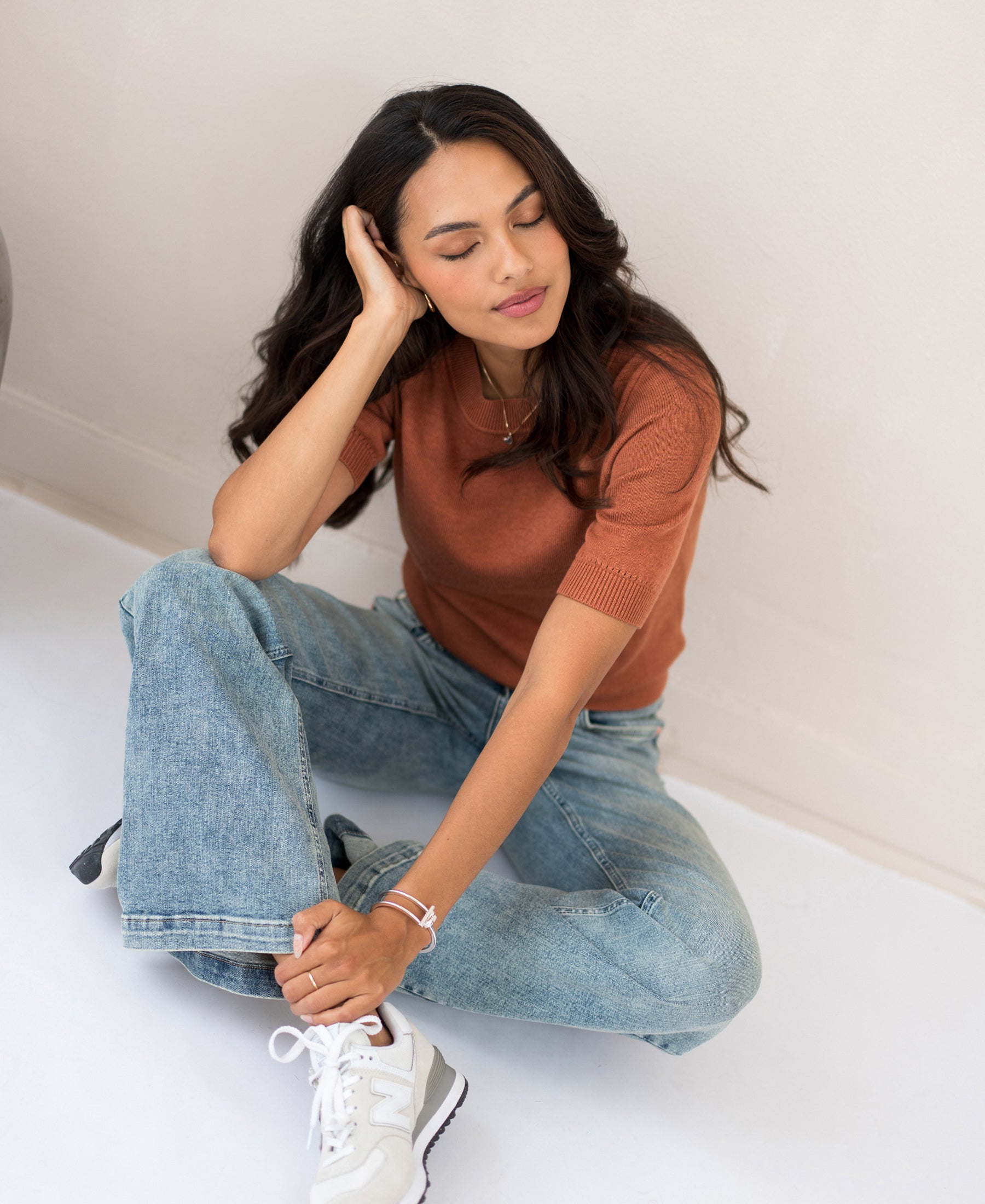 Woman wearing a caramel-colored LA REVE sweater by PLEIN PUBLIQUE sits on the floor with eyes closed.