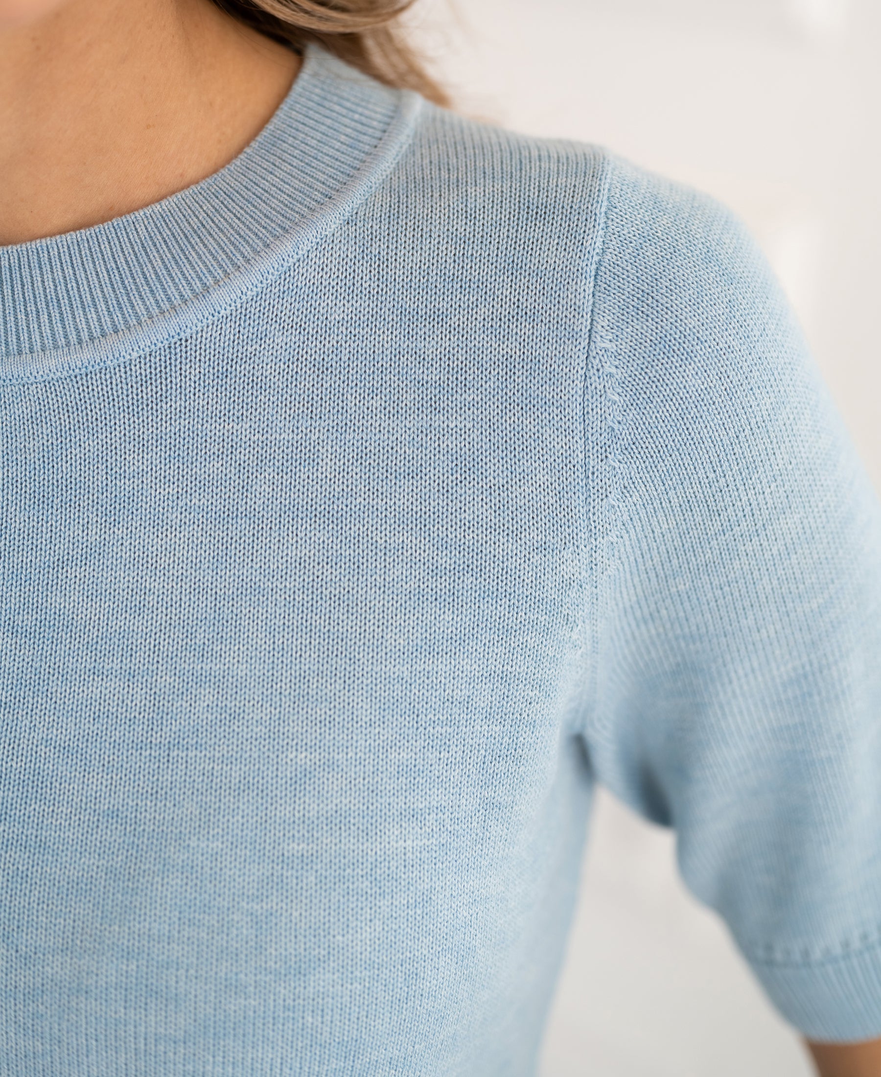 Close-up of a light blue knit sweater with short sleeves and a ribbed crew neck.