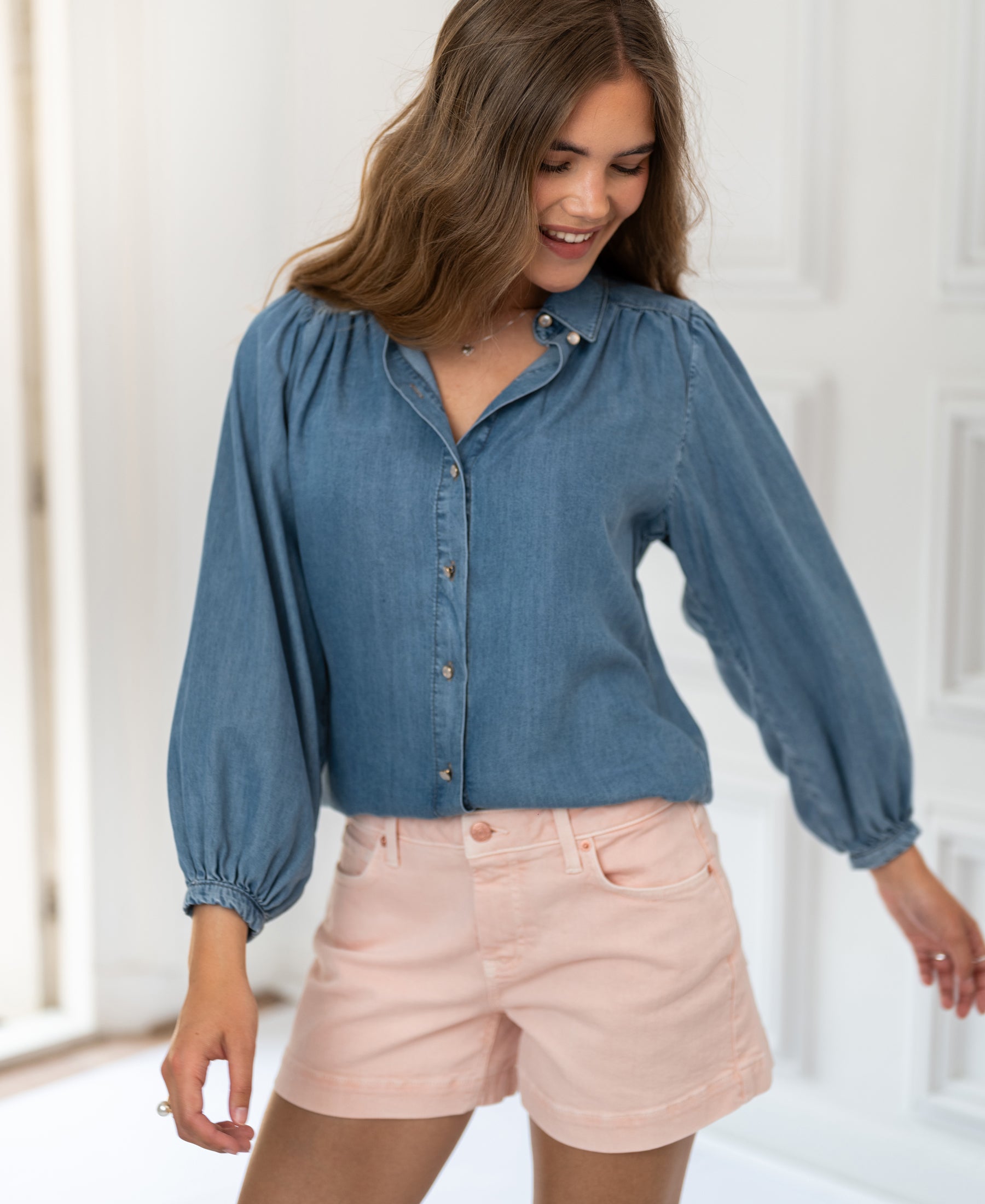 Woman wearing a light blue Tencel denim blouse in stonewash, shown in a bright, airy room.