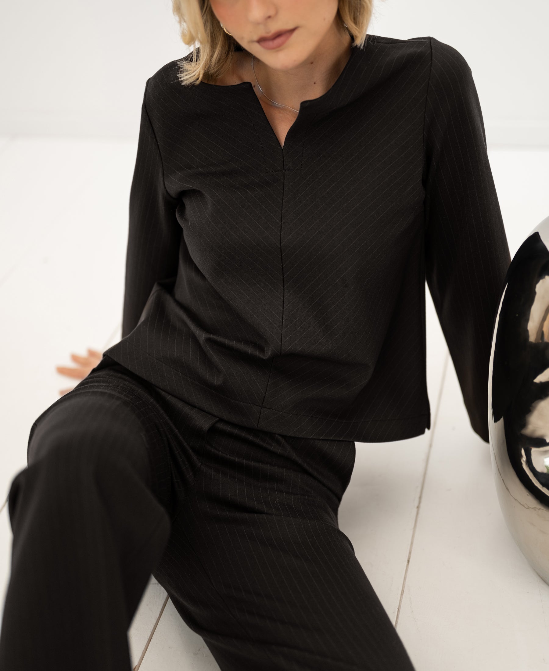 Brown pinstripe LE SAINT top by PLEIN PUBLIQUE, shown on a model sitting on a white floor.