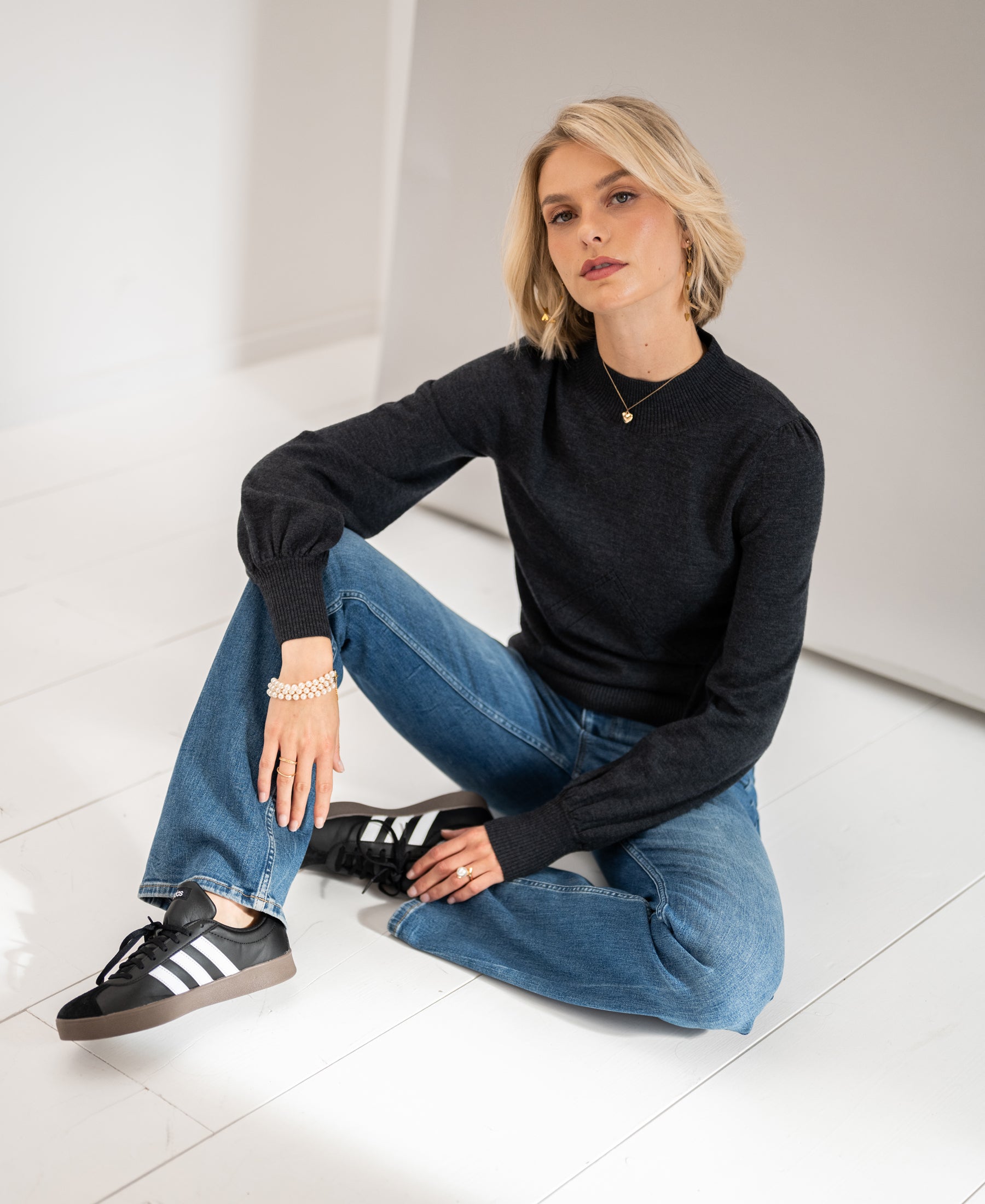 Woman wearing a PLEIN PUBLIQUE charcoal turtleneck sweater standing on a white floor.