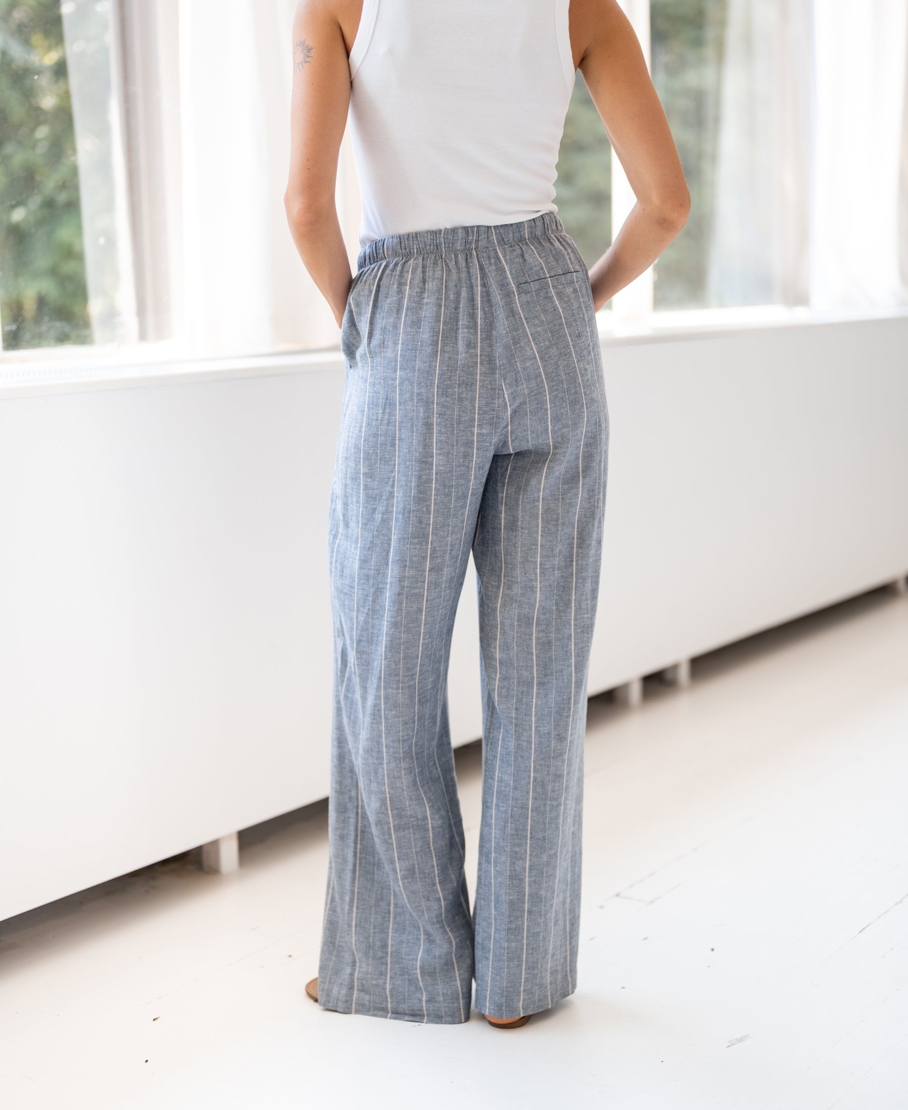 Striped linen-blend LA SECONDE trousers in jeans blue by PLEIN PUBLIQUE, shown worn by a woman.