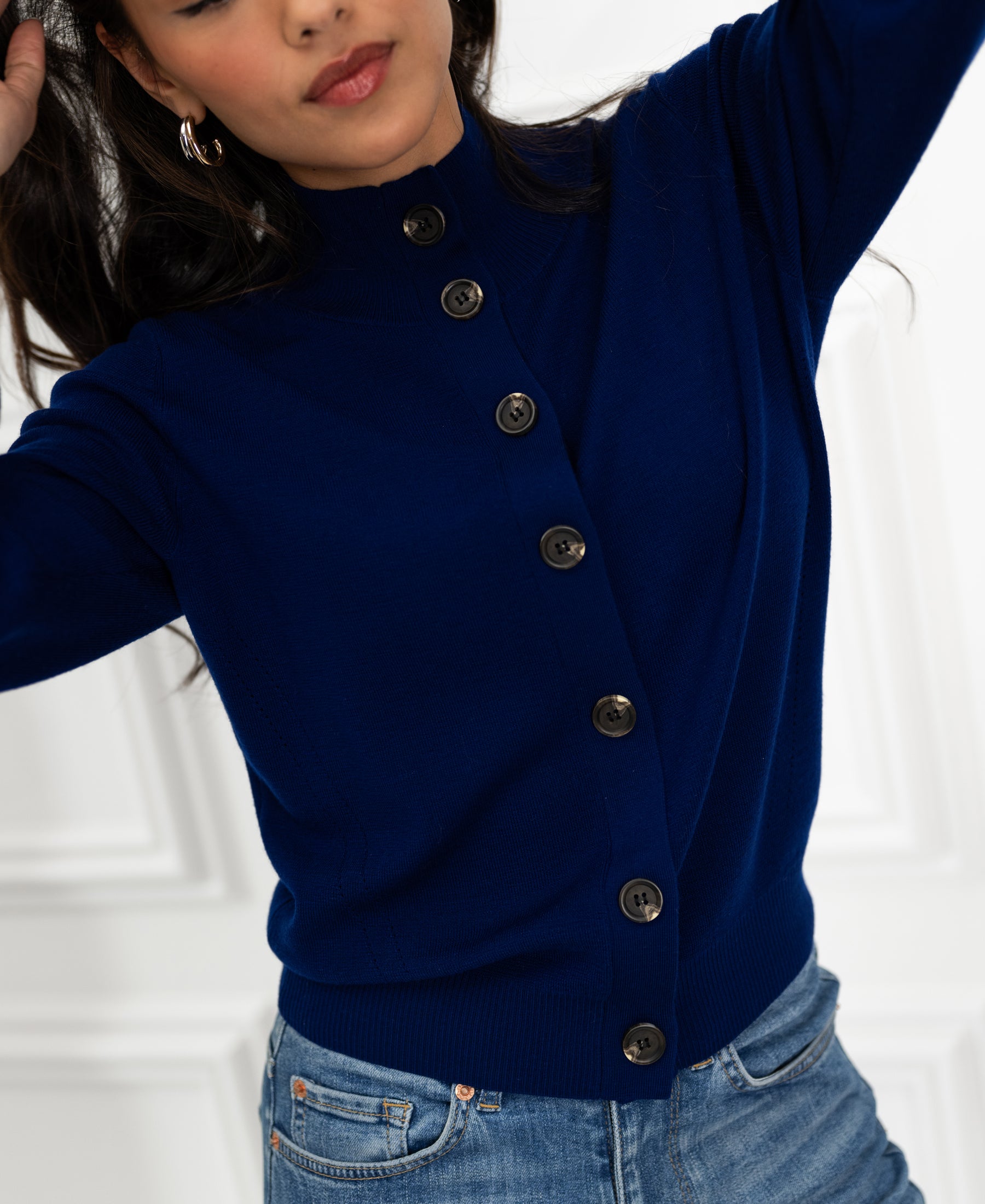 Navy blue merino turtleneck cardigan by PLEIN PUBLIQUE, shown on model with arms raised against a white background.