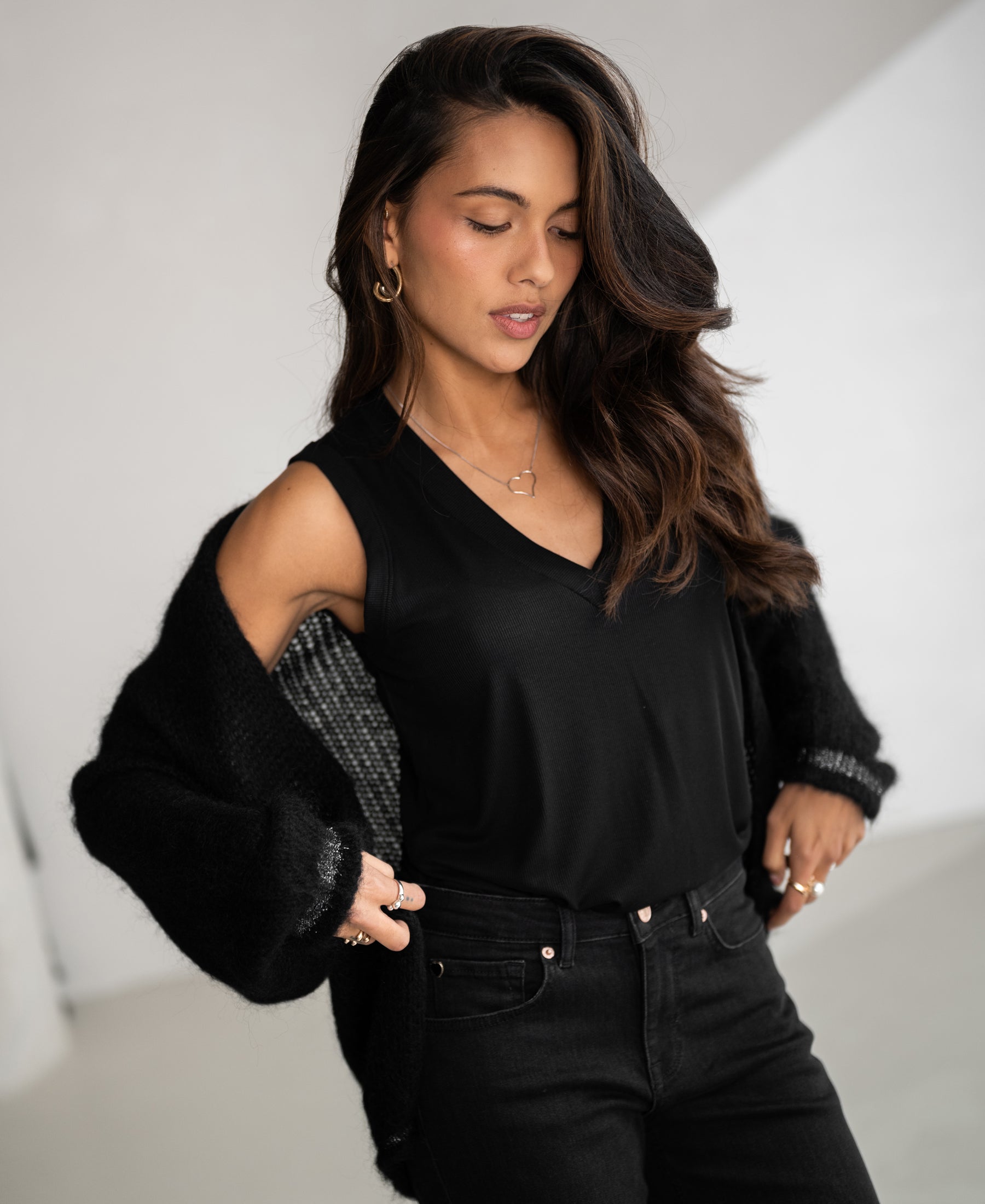 Black Lyocell top by PLEIN PUBLIQUE shown indoors, modeled with one hand on hip; the model is looking down and smiling.