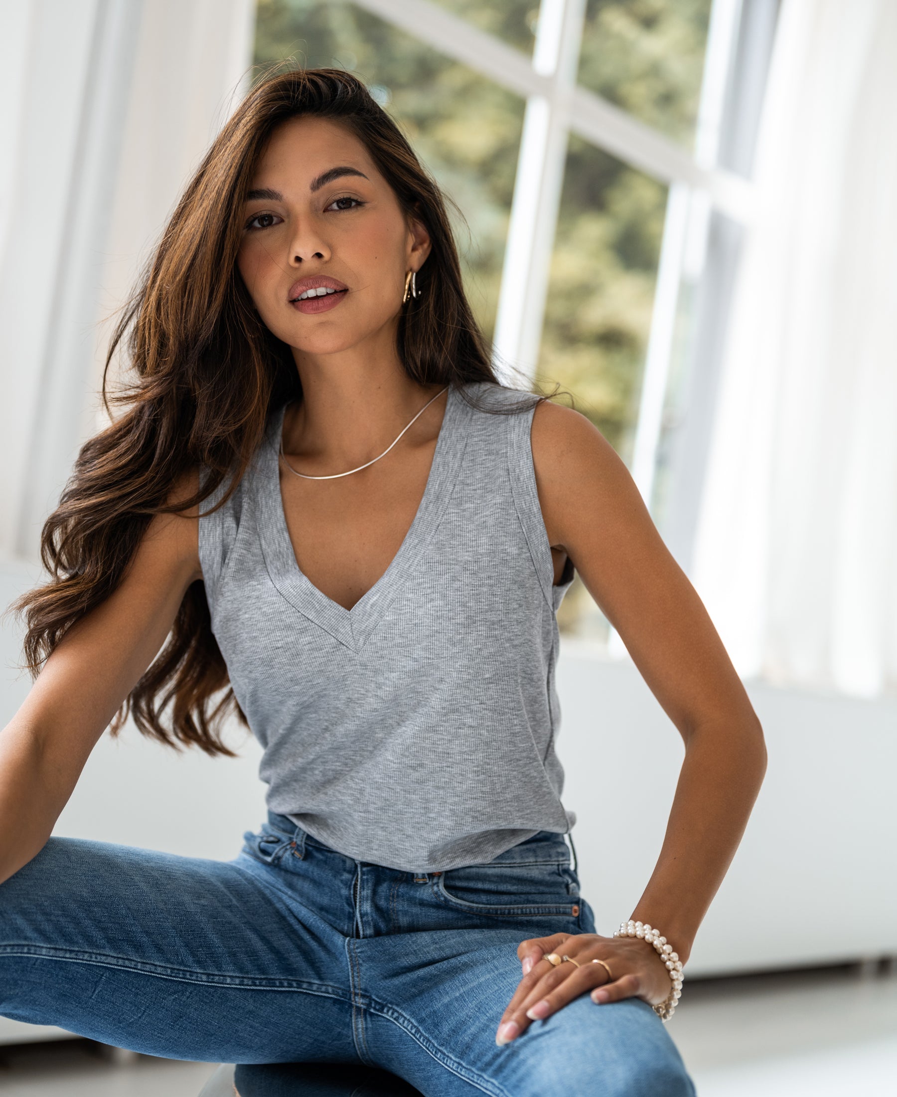 Woman wearing a grey melange Lyocell top sits by a bright window, facing the camera.