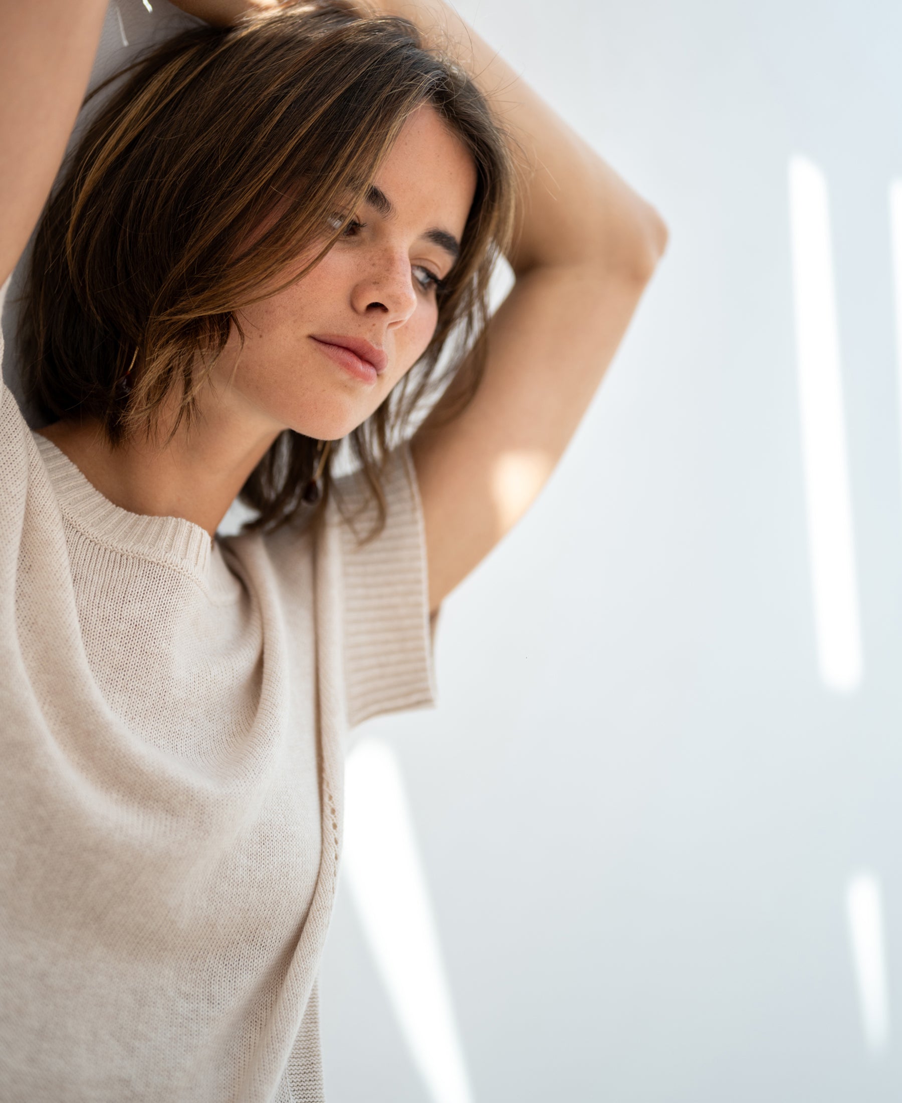 Light sand-colored linen summer sweater, PLEIN PUBLIQUE LE SOLEIL, shown with models arms raised in sunlight.